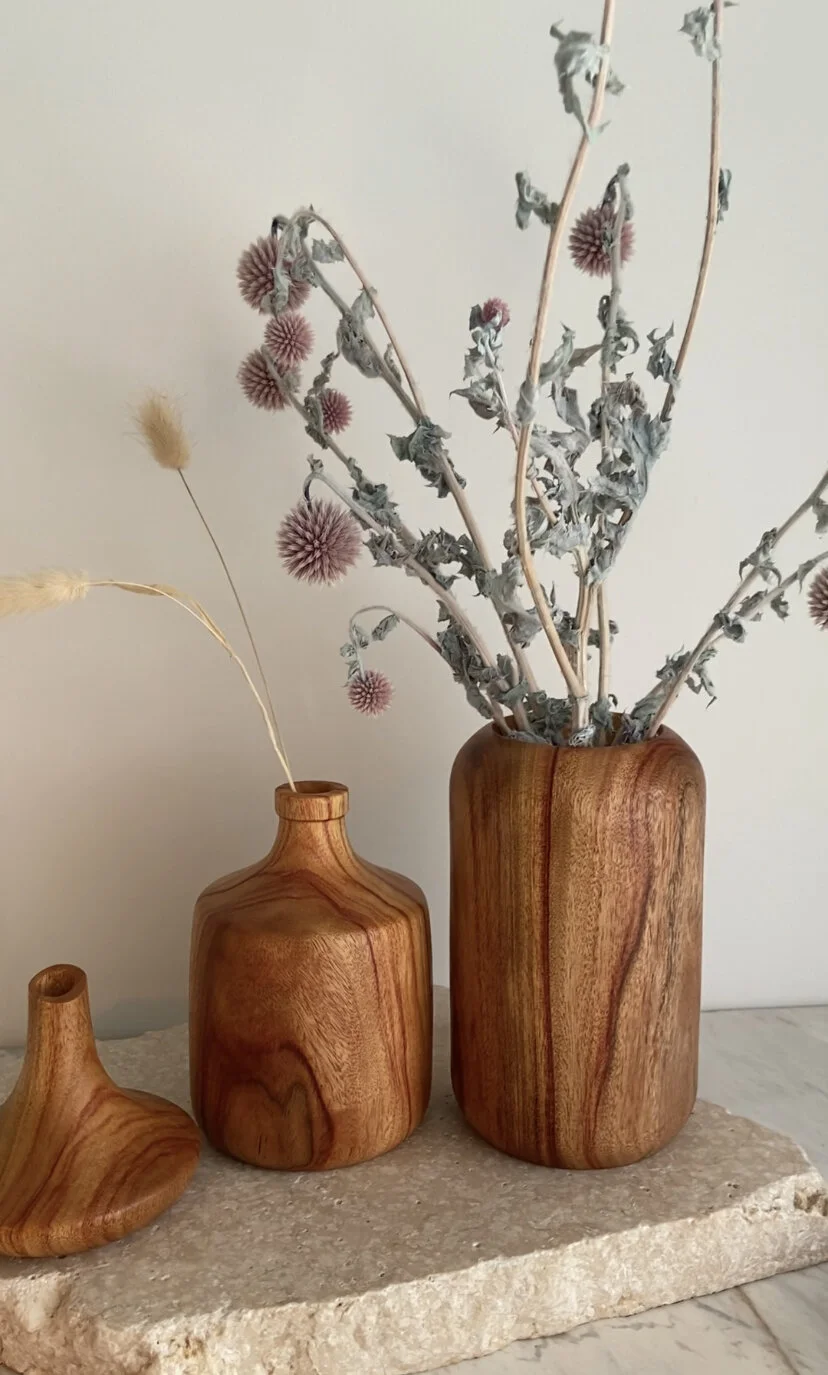 Three wooden vases with dried plants on a stone slab, against a plain background.