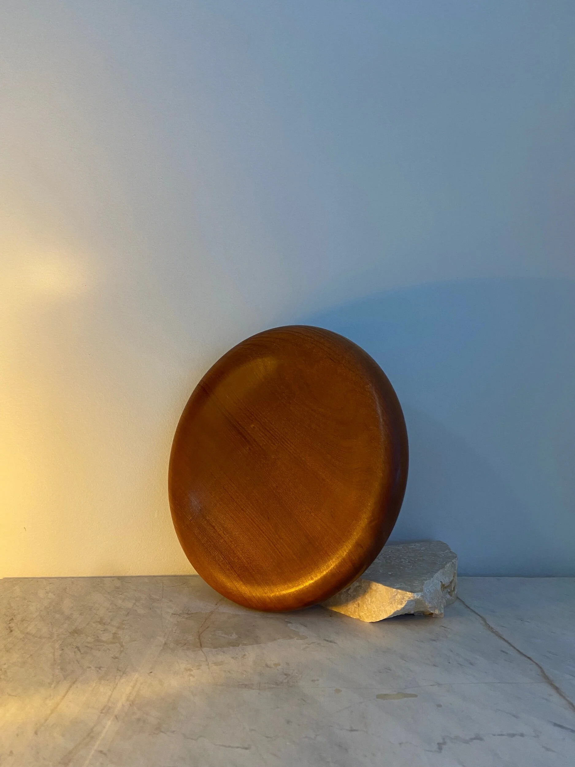 A round, polished, copper-colored object resting on a small piece of rock on a light-colored surface, with a light-colored background.