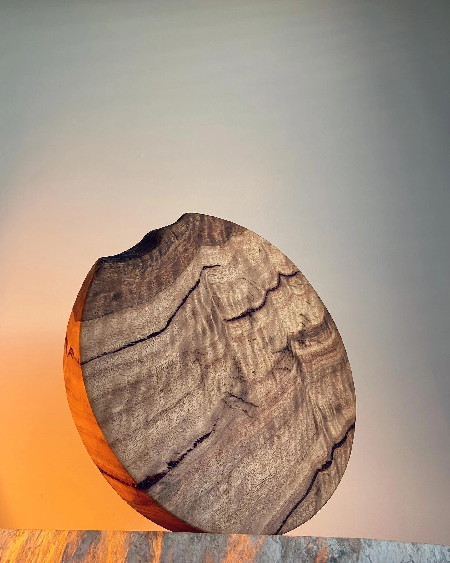 A round wooden sculpture with natural wood grain and dark lines, set against a clear sky at sunset.