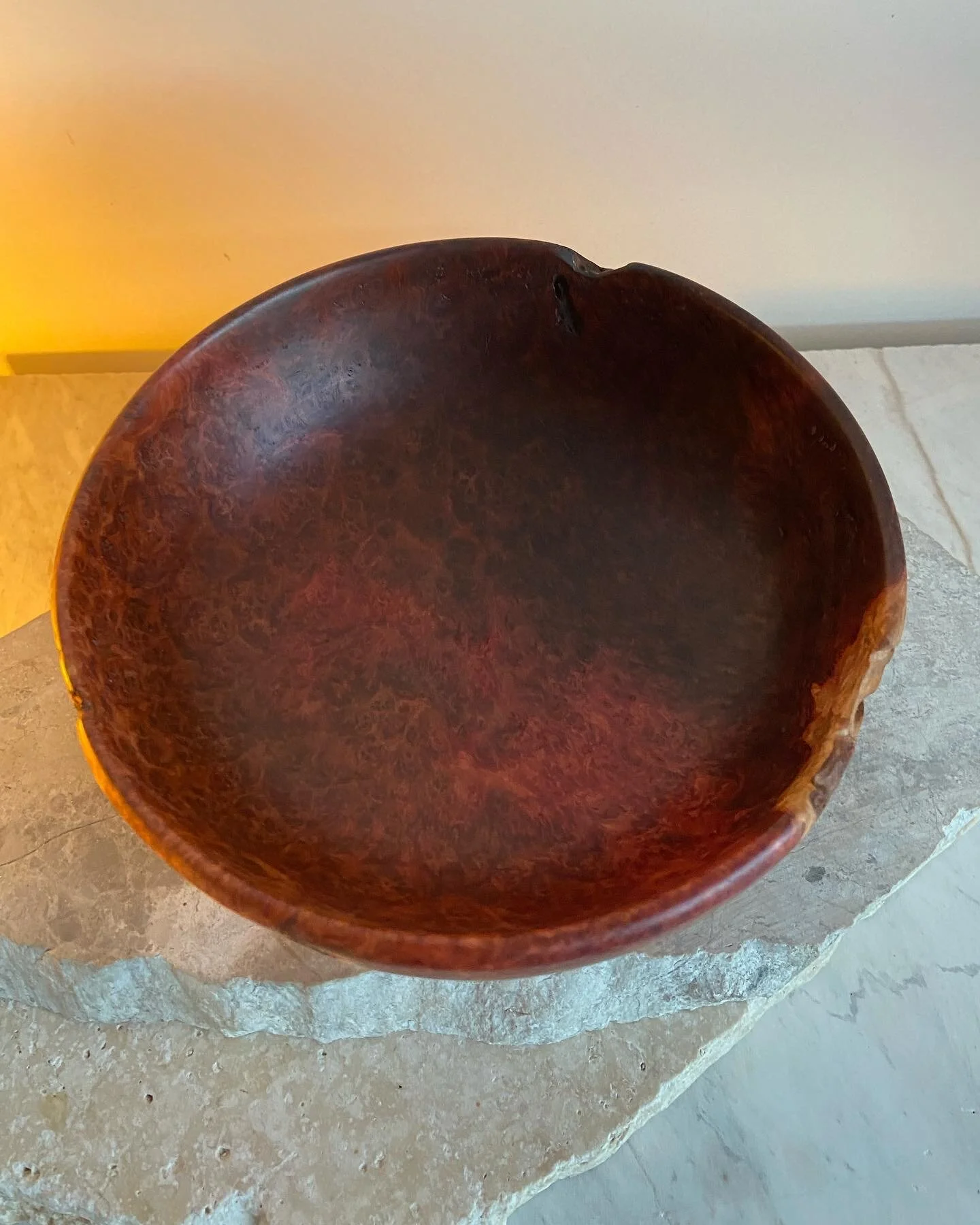 A round wooden bowl with a smooth, polished surface sitting on a stone surface.