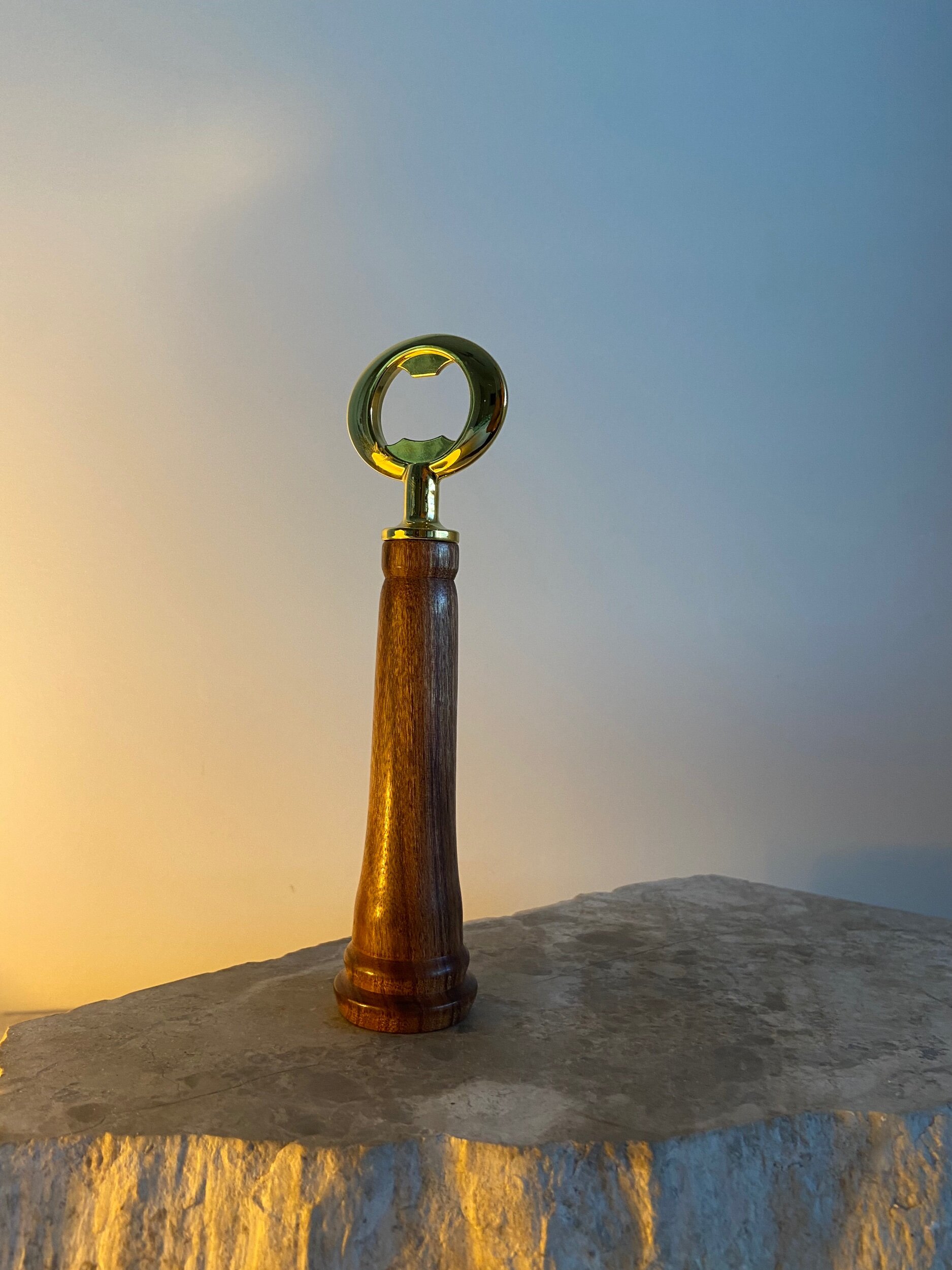 A bottle opener with a wooden handle and a metallic end, placed on a stone surface against a gradient background of yellow and blue.