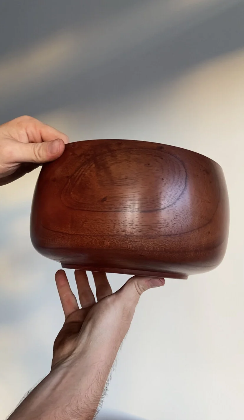 Two hands hold a polished wooden bowl against a cloudy sky background.