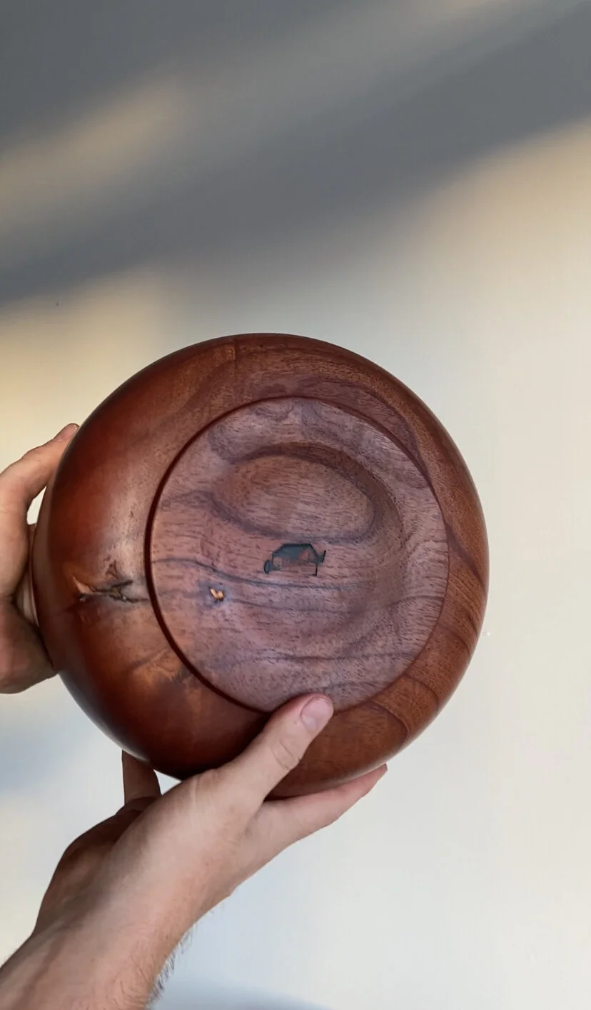 A hand holding a round wooden bowl against a neutral wall background.