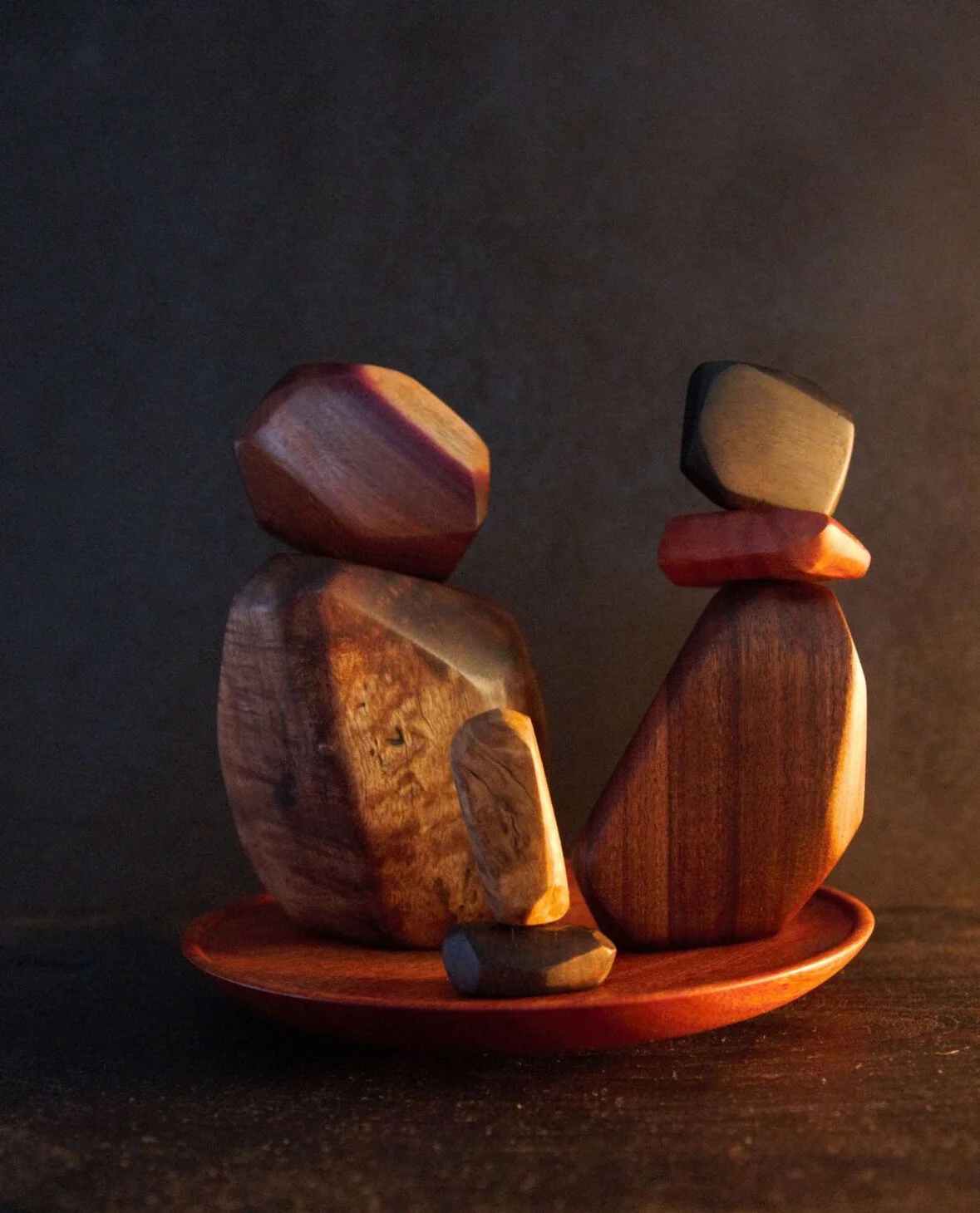 Three wooden abstract sculptures on a small round wooden plate against a dark background.
