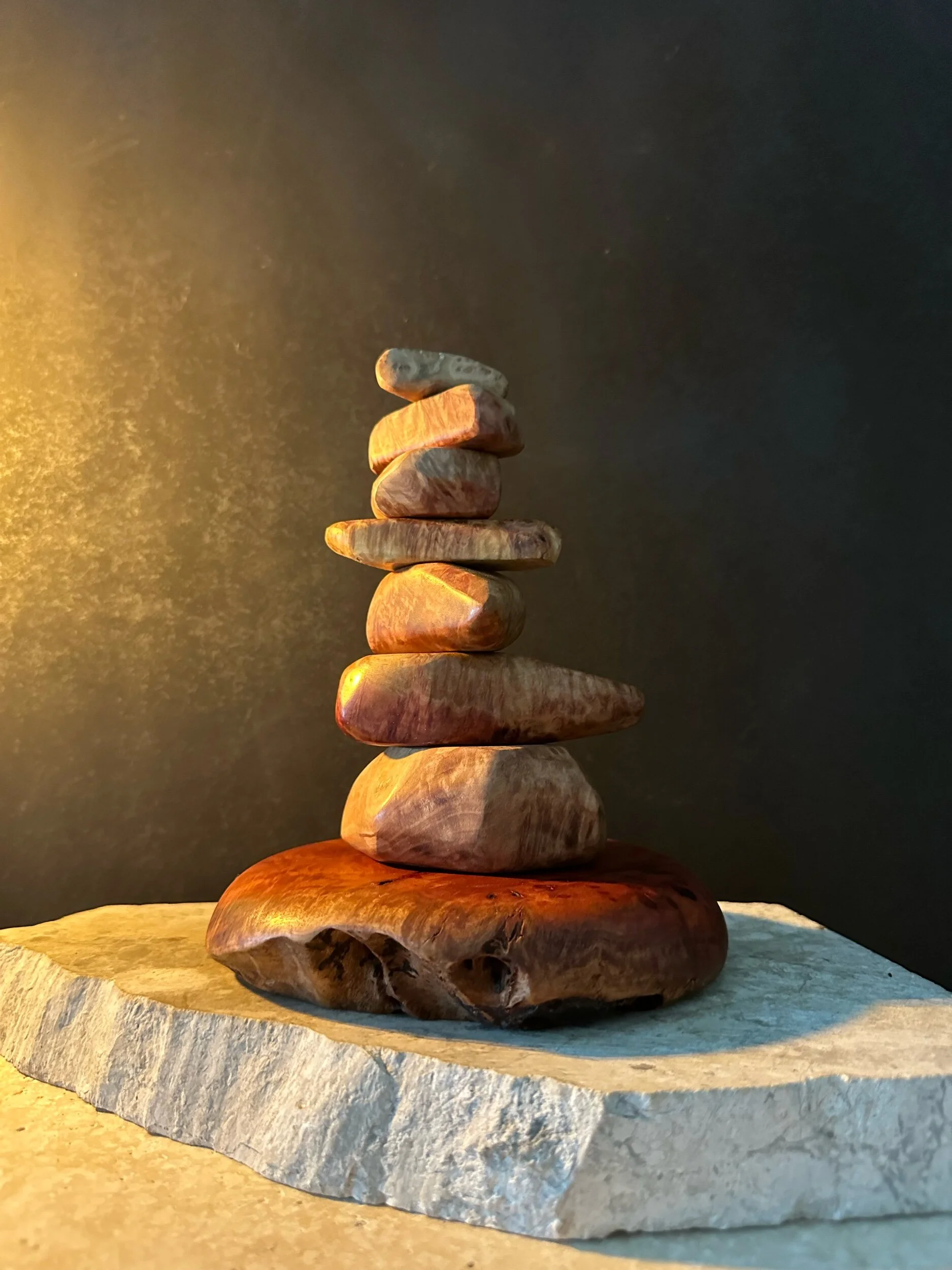 A stack of various-sized smooth stones placed on a flat, wide stone slab with a dark background.