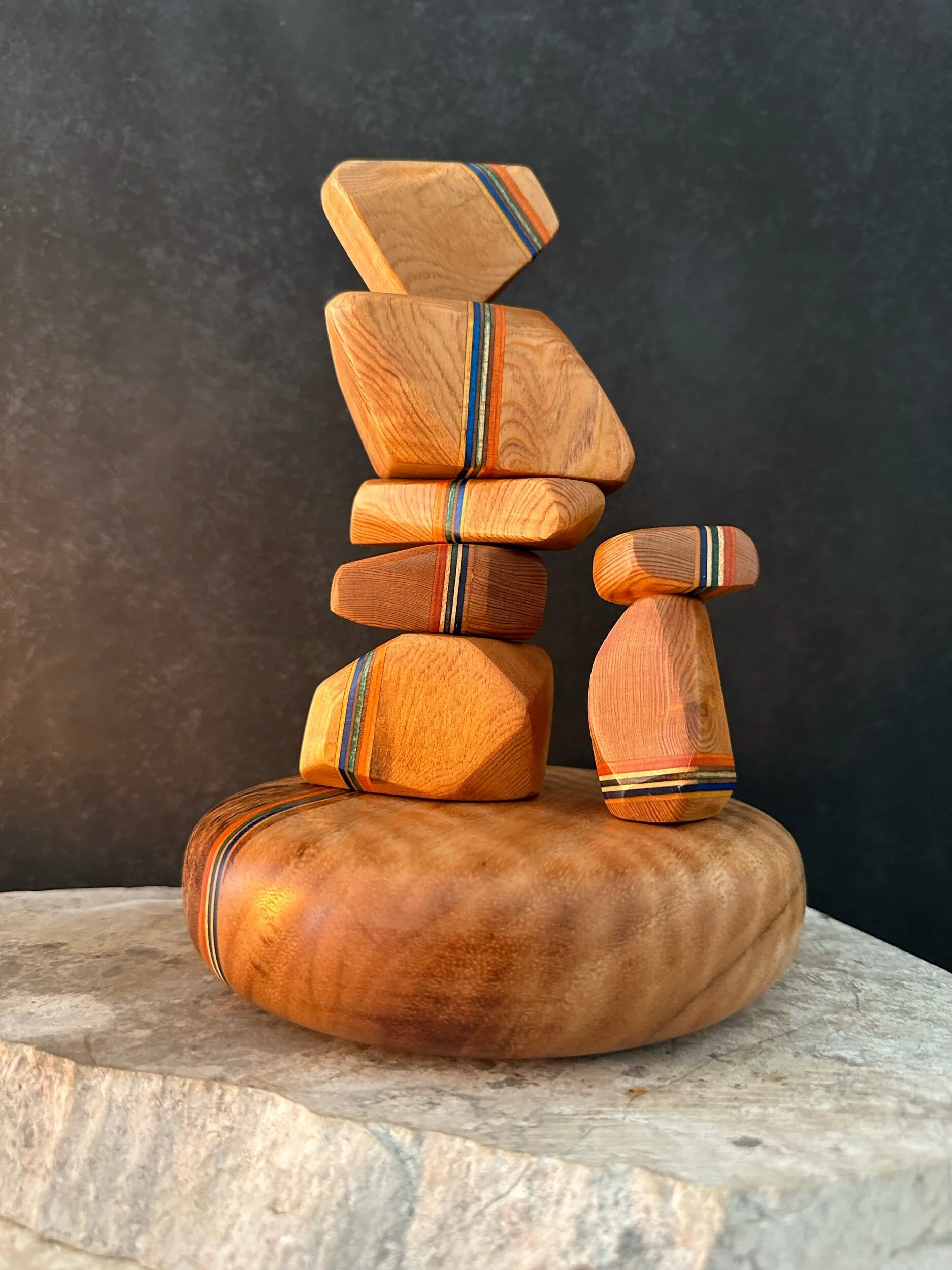 Stacked decorative wooden stones with colorful stripe patterns placed on a stone surface against a dark background.