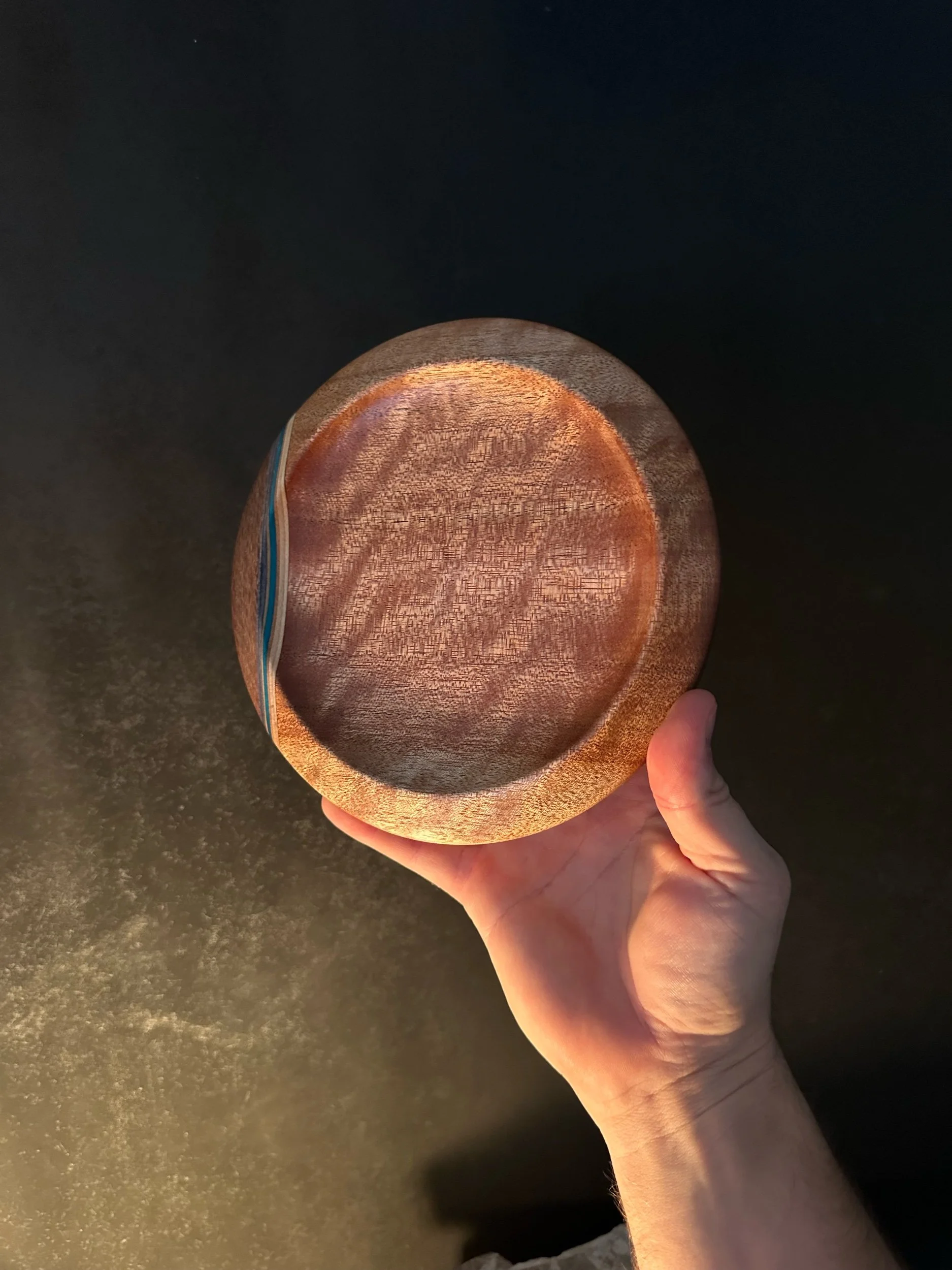 A person holding a round, wooden bowl against a dark background.