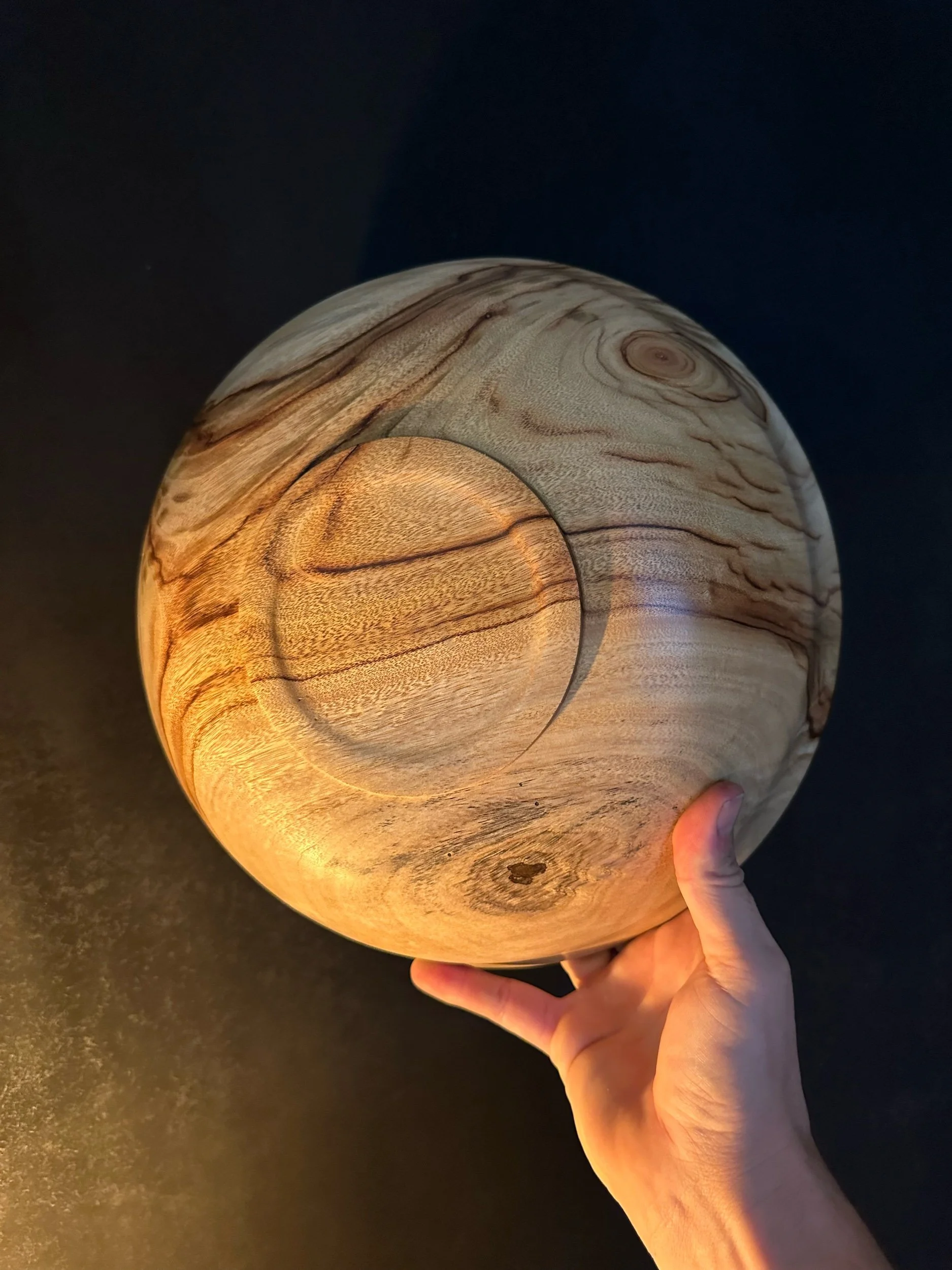 A wooden light fixture with a sphere shape, glowing warmly and being held by a person's hand.