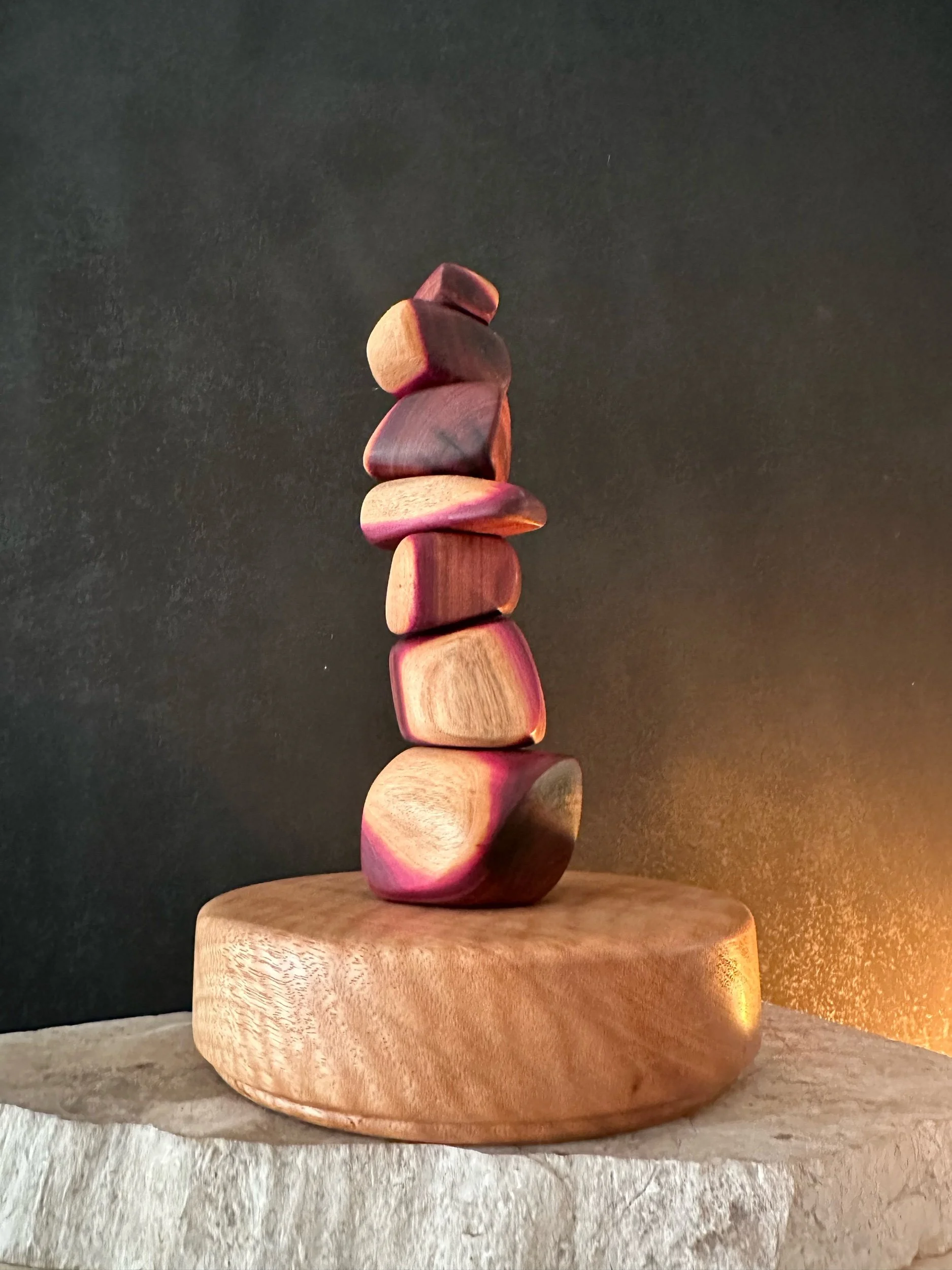 Stacked pink and brown wooden stones on round wooden base against dark background