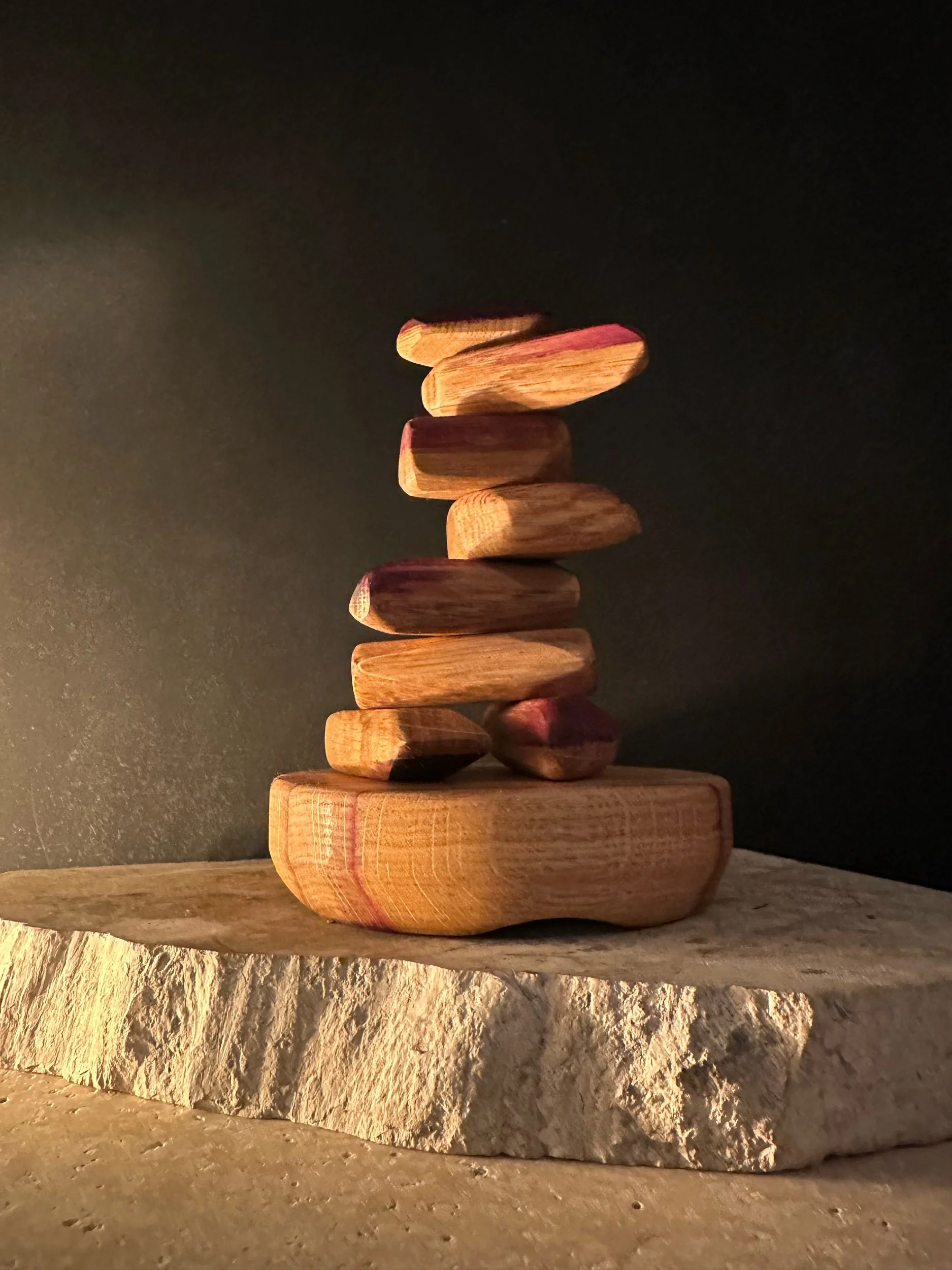 Stacked small wooden pebbles or pieces on a rough stone surface against a dark background.