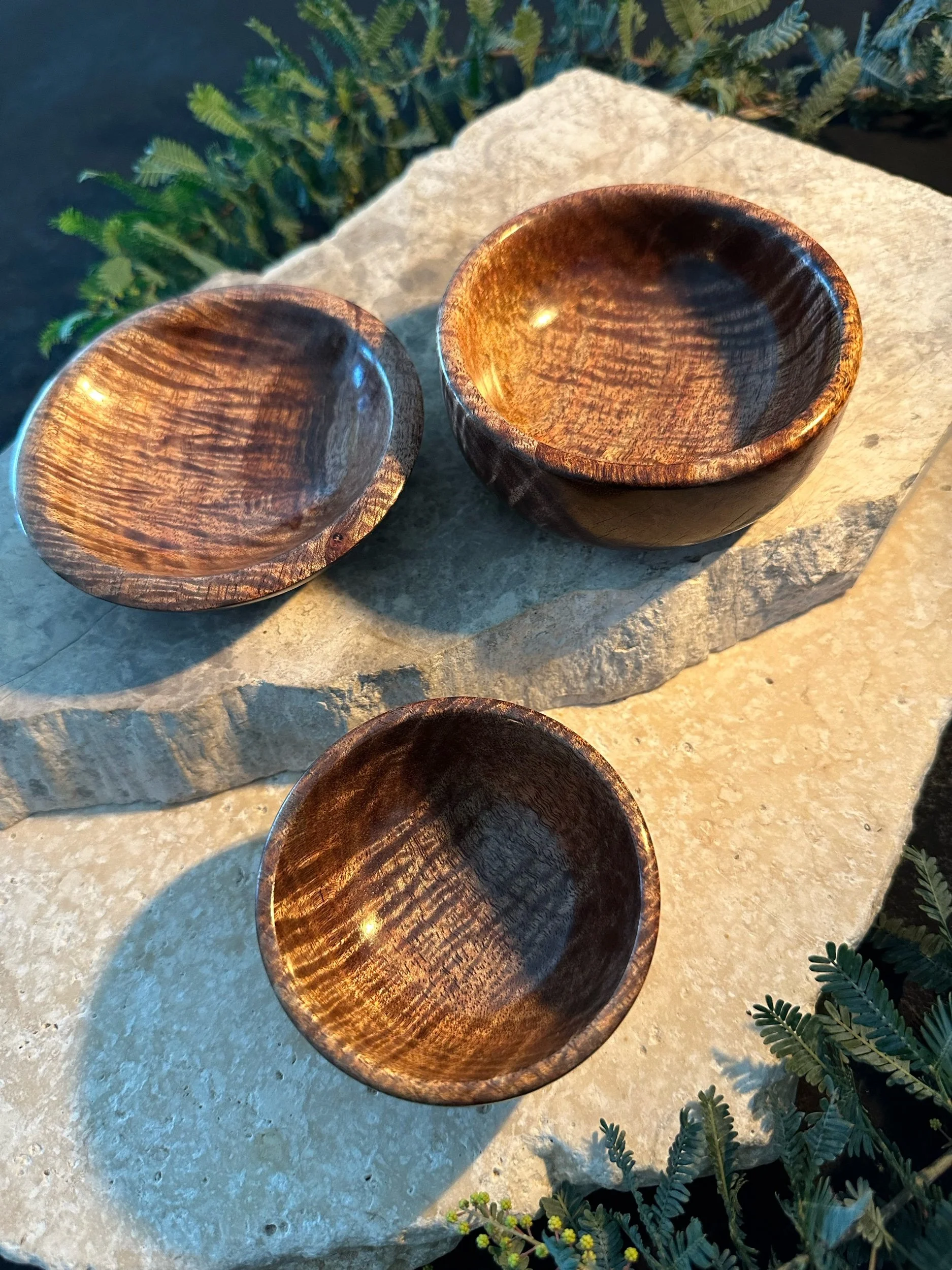 Three wooden bowls on a stone surface surrounded by greenery.