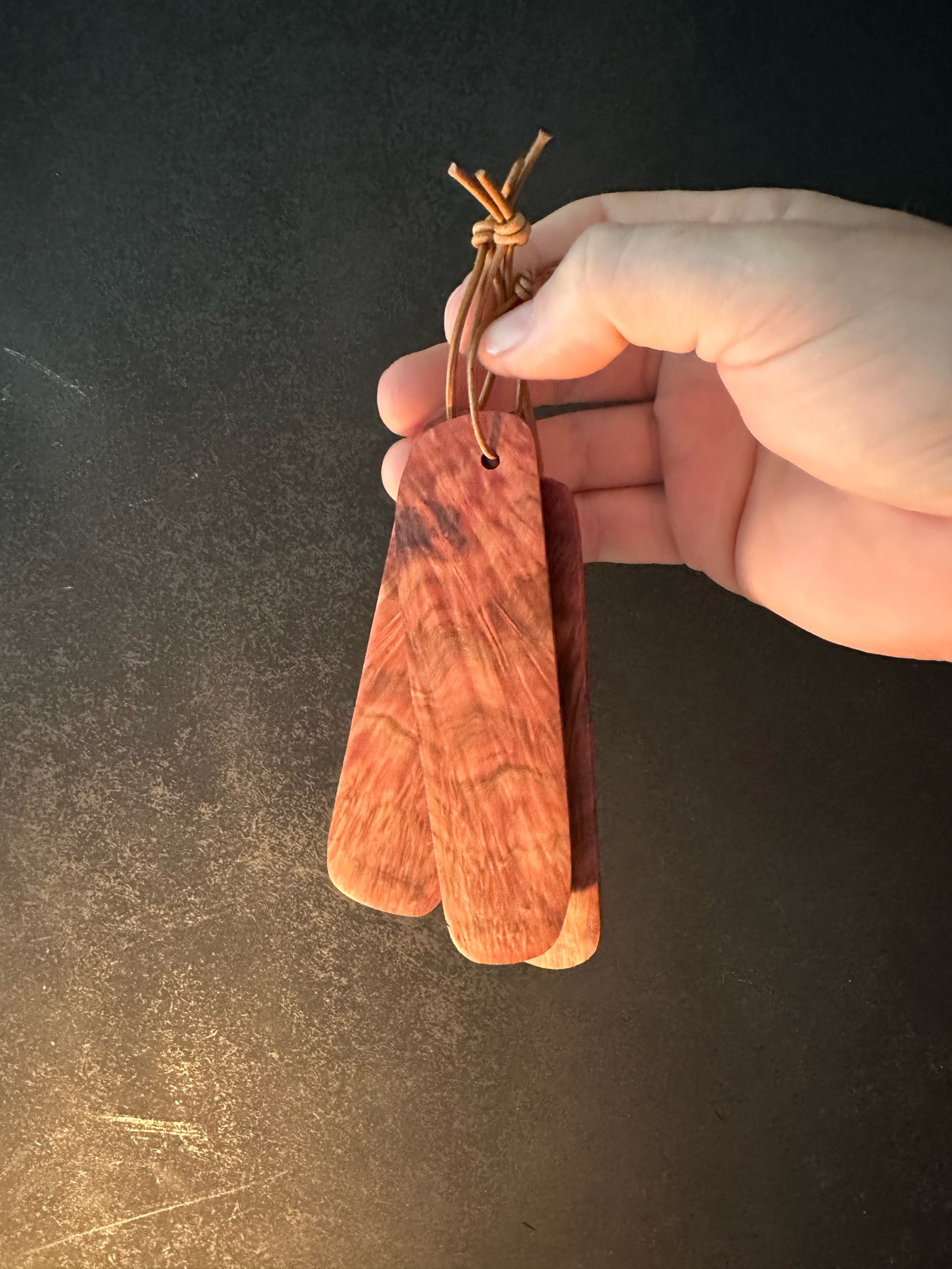 A hand holding three wooden keychains attached to a leather strap, against a dark background.