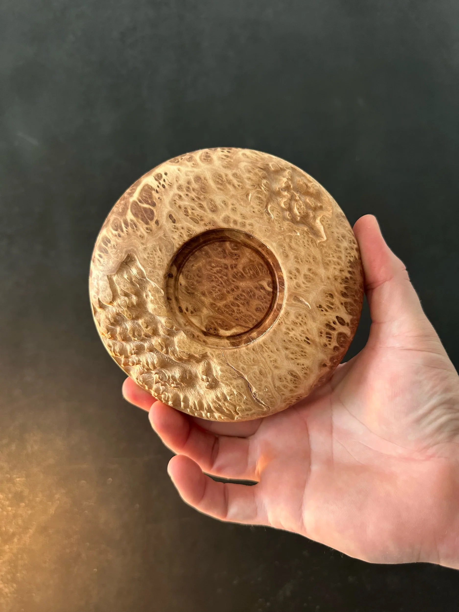 Hand holding a round wooden bowl with a rustic, textured surface on a black background.