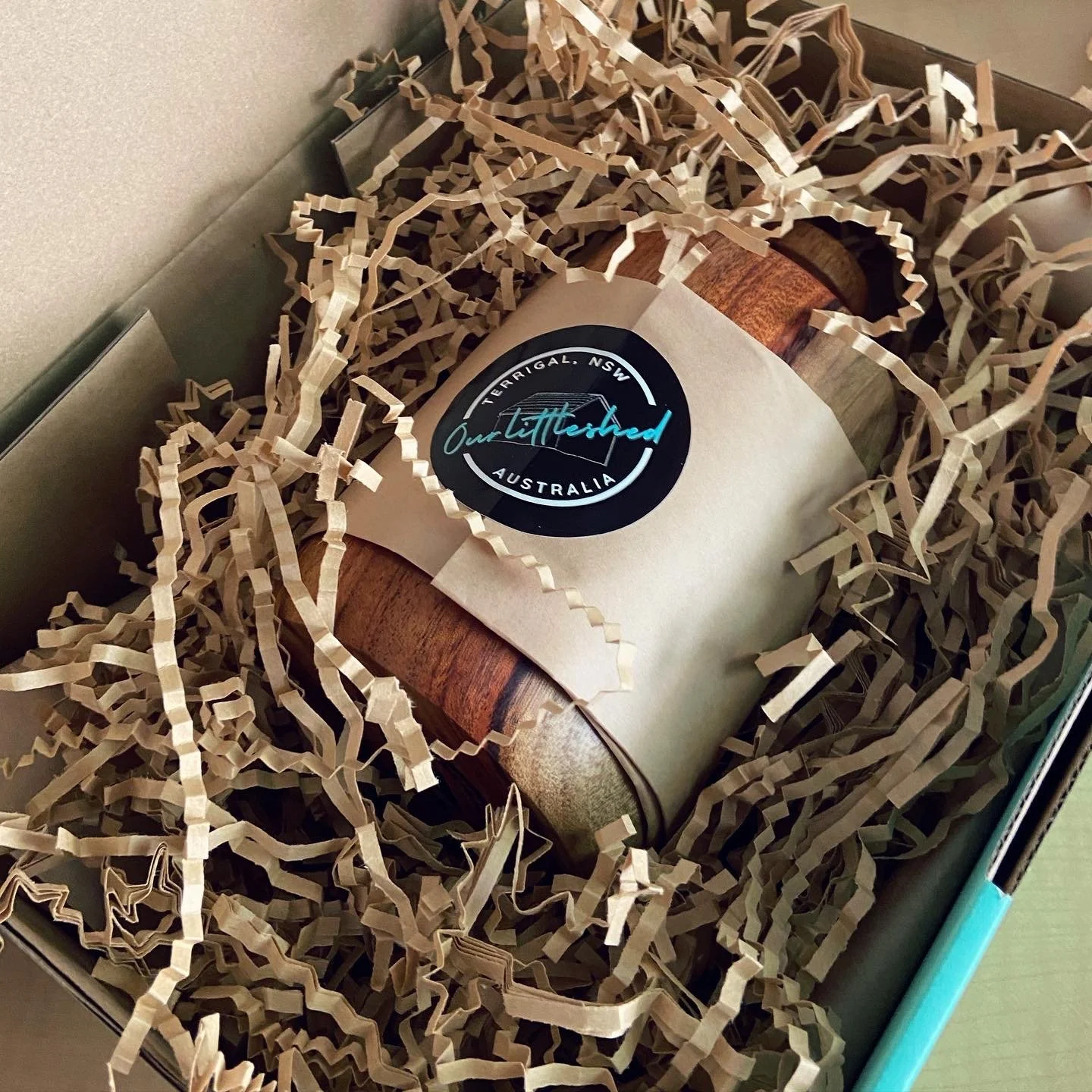 Gift box filled with shredded paper, containing a wrapped item with a circular sticker that says 'Our Littleshed, Terrrigal NSW, Australia'.