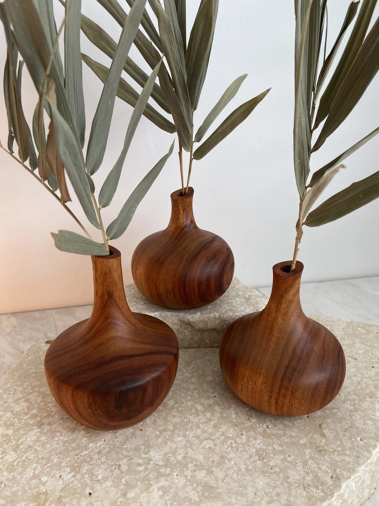Three wooden vases with dried gray-green leaves on a textured beige surface.