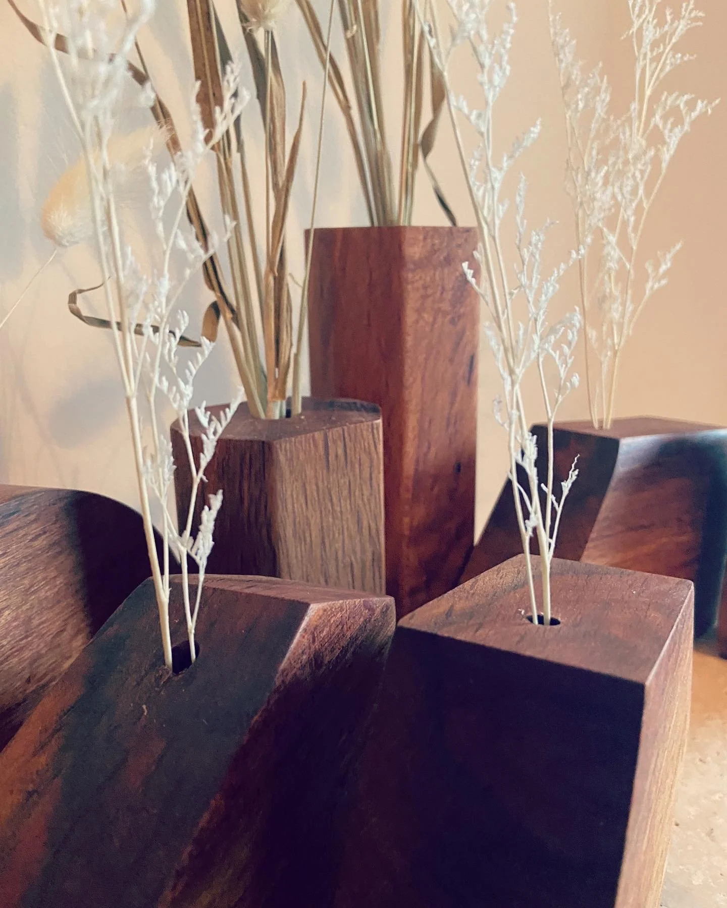 Close-up of four wooden vases with dried branches on a light-colored surface.