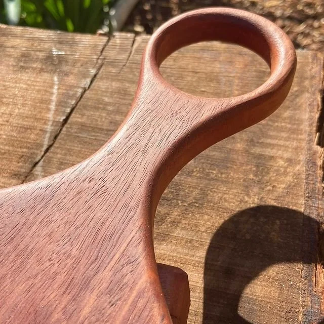 A wooden handle or paddle with a circular hole at the top, placed on a wooden surface outdoors.