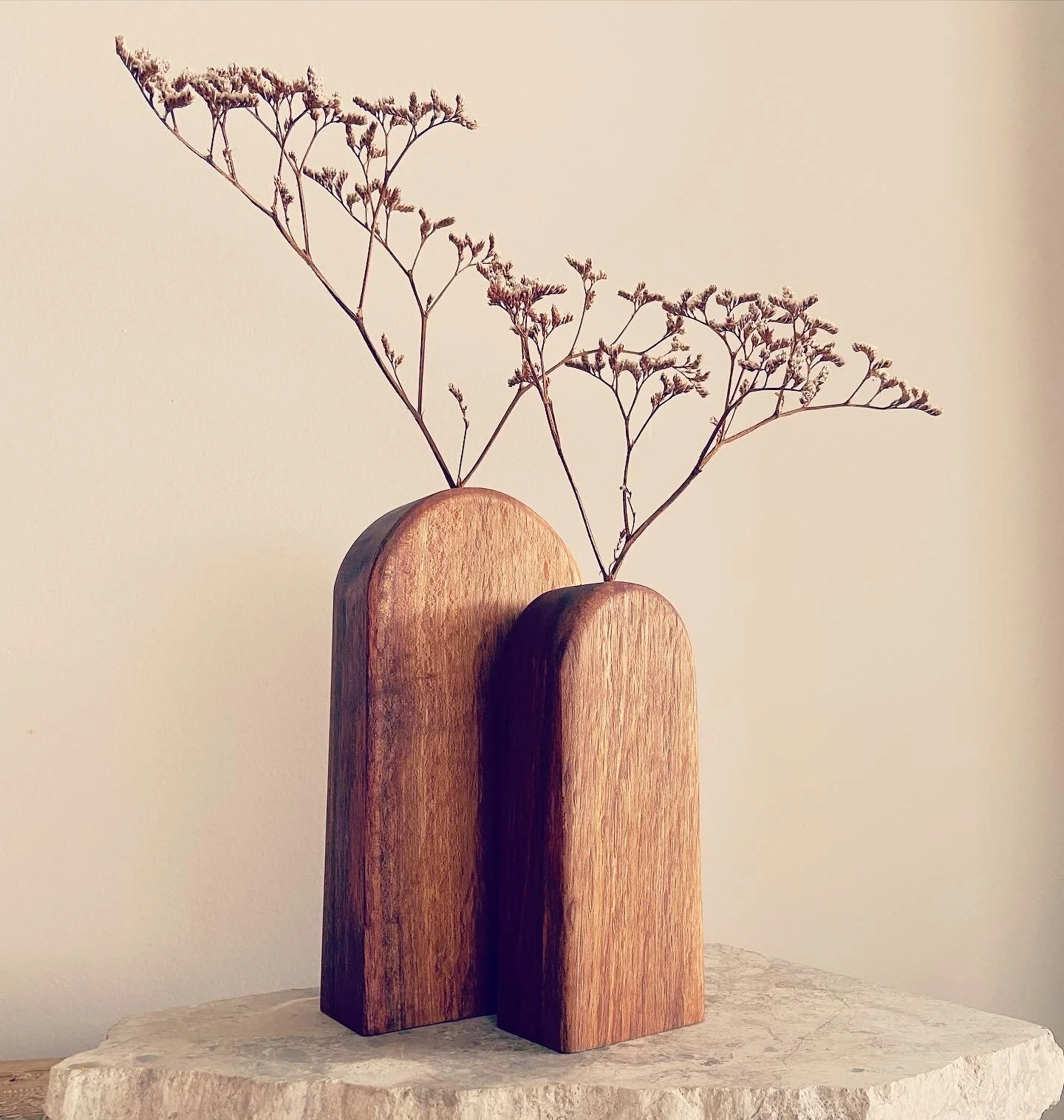 Minimalist wooden vases with dried branches on a textured surface against a plain wall.