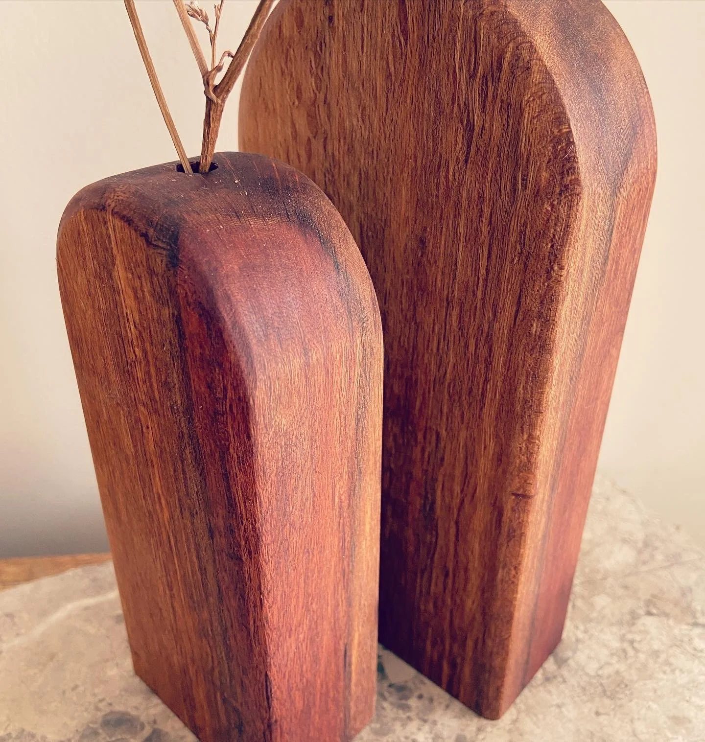 Two wooden sculptures or objects with rounded tops and elongated shapes, placed on a stone surface.