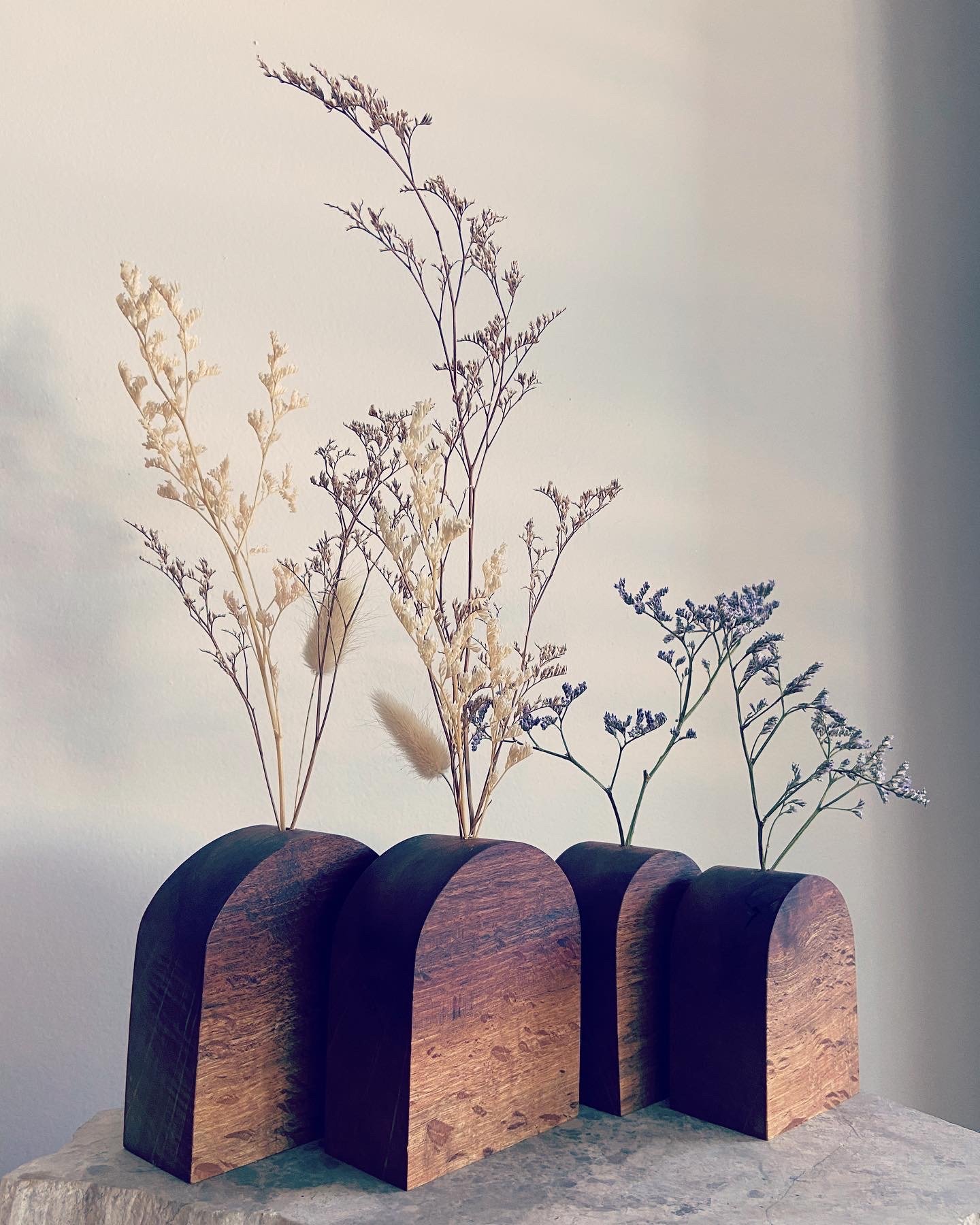 Decorative arrangements of dried flowers in wooden semi-circular holders on a stone surface.