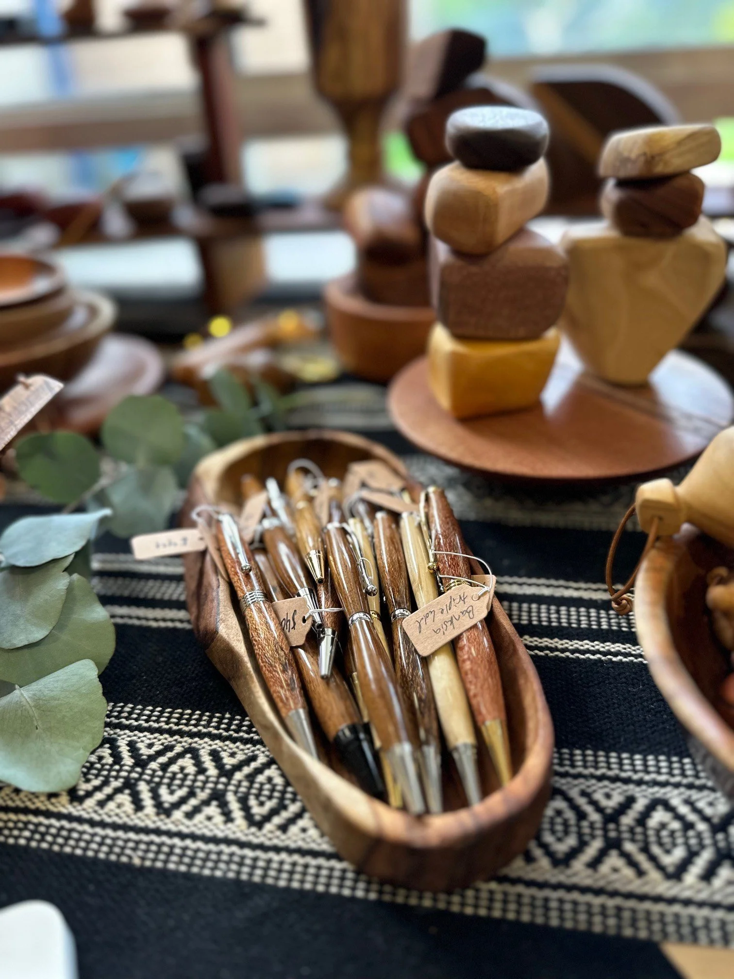 Wooden pens displayed in a wooden tray on a patterned cloth at a craft fair.