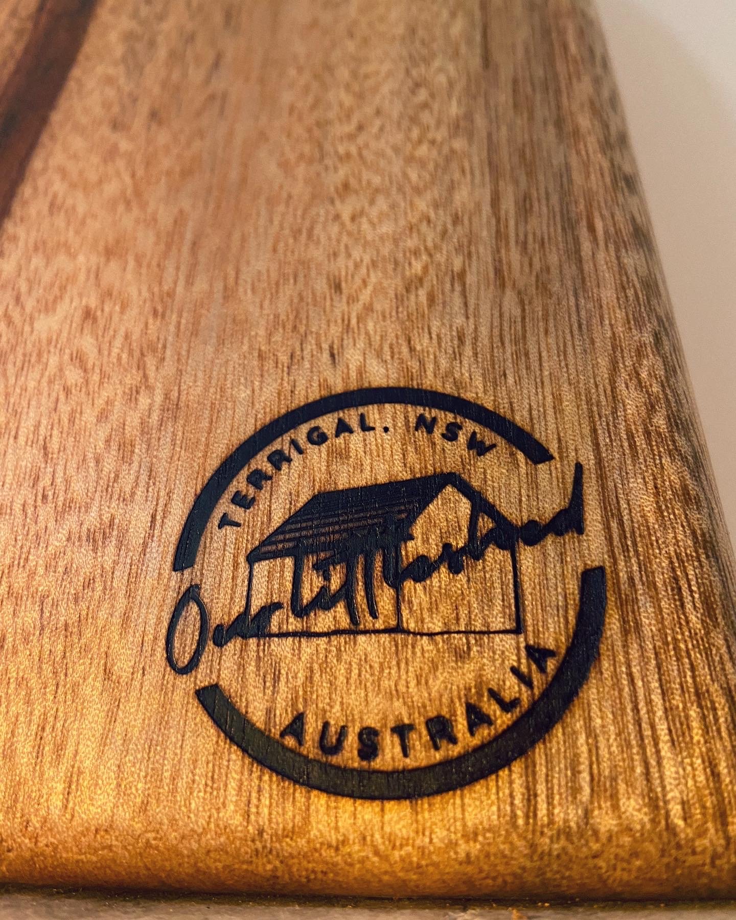 Close-up of a wooden object with a black stamped logo reading 'Terrigal, NSW, Australia' and a mountain and hut illustration.