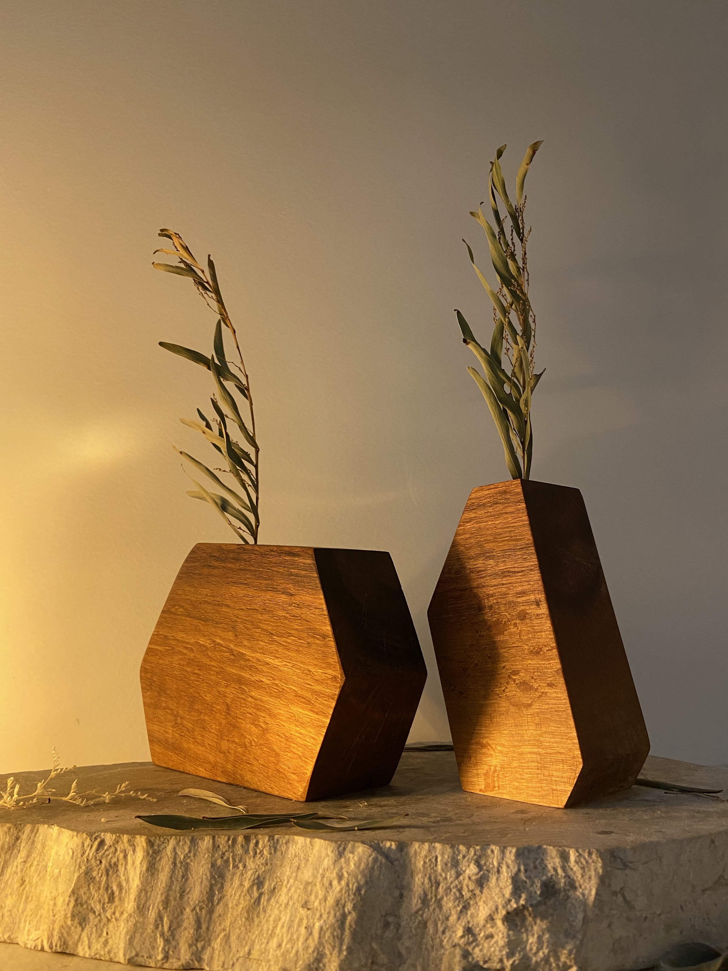 Two wooden vases with olive branches on a stone surface, illuminated by warm lighting.