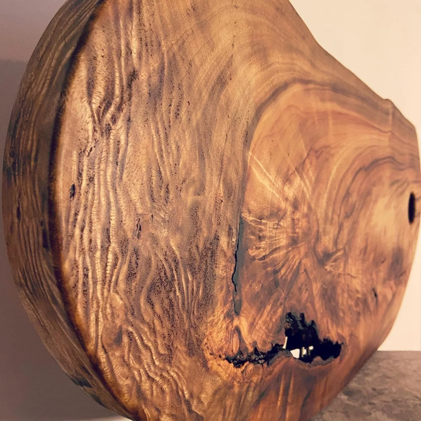 Close-up view of a wooden sculpture or table with a natural, polished surface showing wood grain, rings, and a large knot or opening.