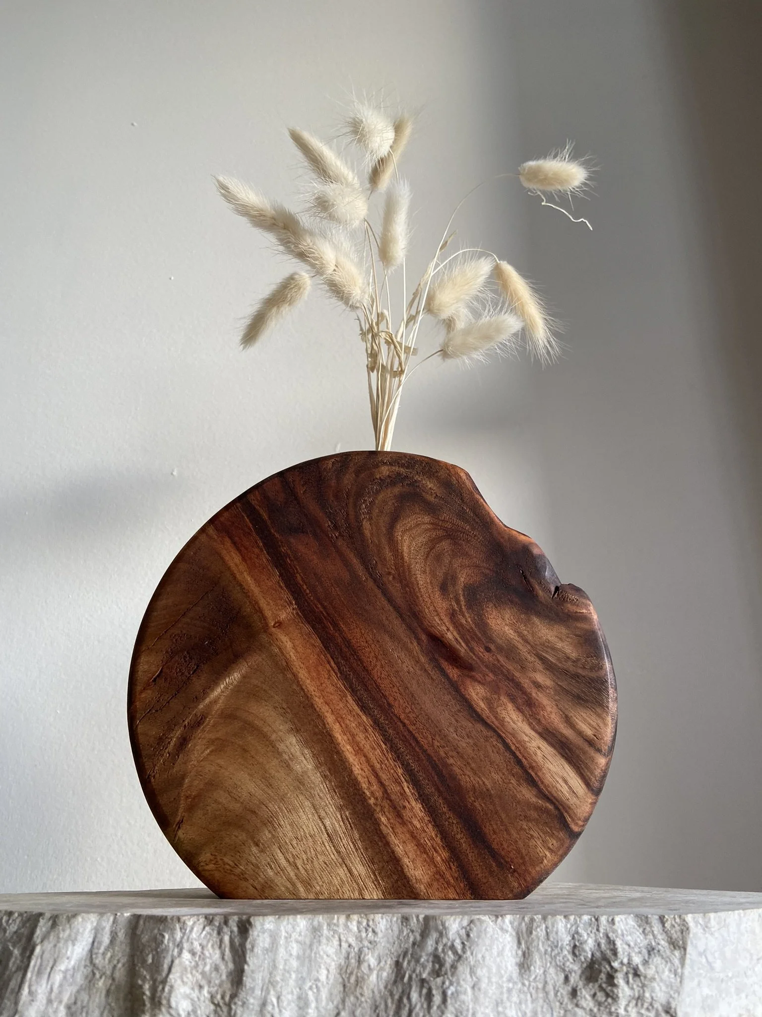 Decorative wooden vase holding dried white grass stalks on a textured surface