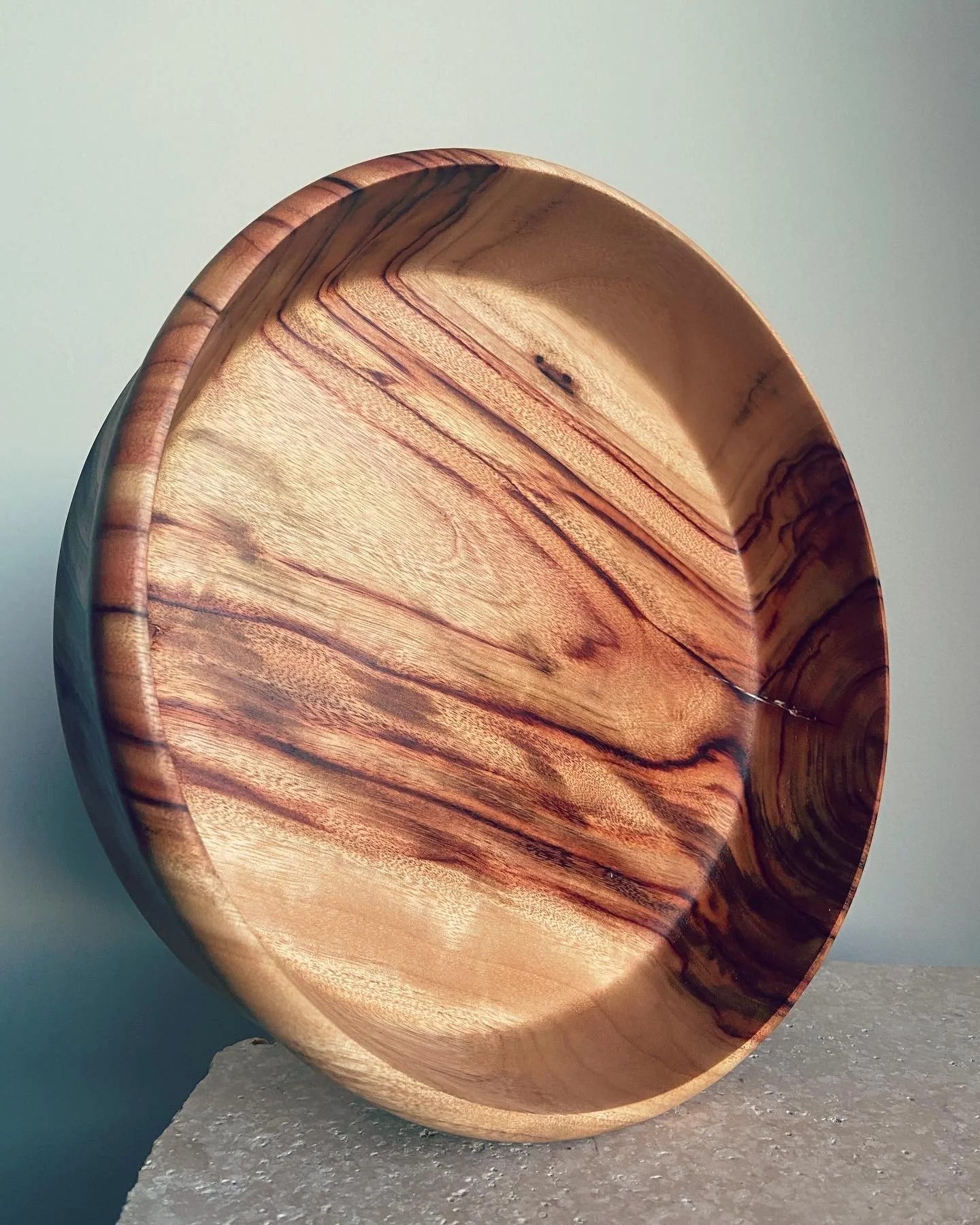 A polished wooden bowl with natural grain patterns, placed on a textured surface against a plain background.