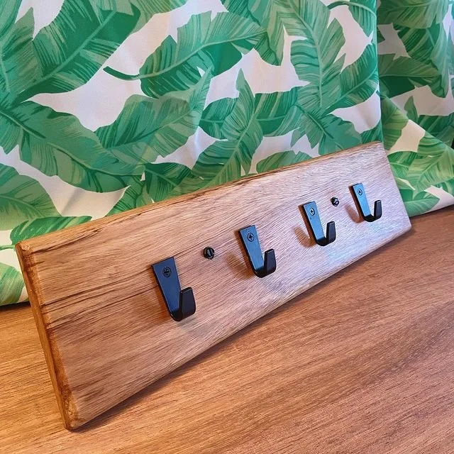 Wooden wall hook rack with five black hooks in front of a green, leafy wallpaper background.
