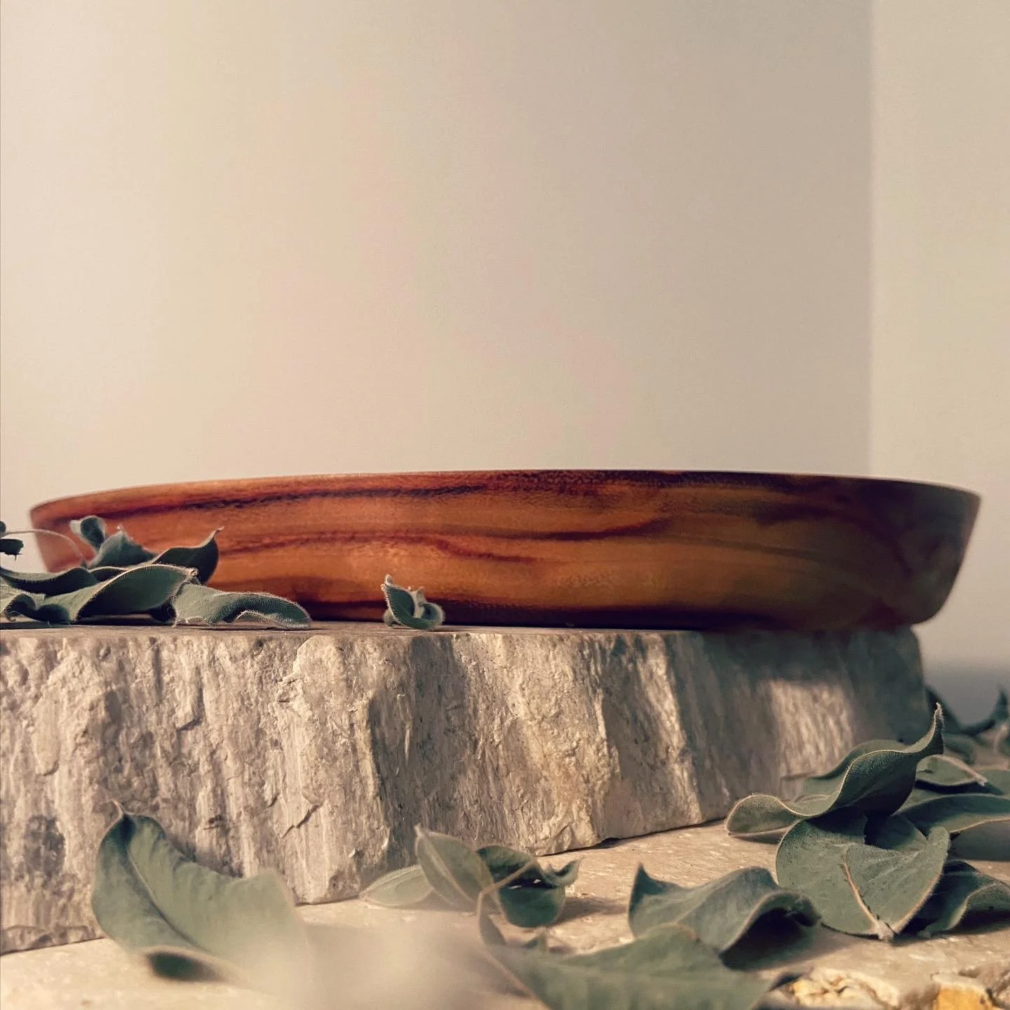 A wooden bowl resting on a textured stone surface with eucalyptus leaves scattered around.