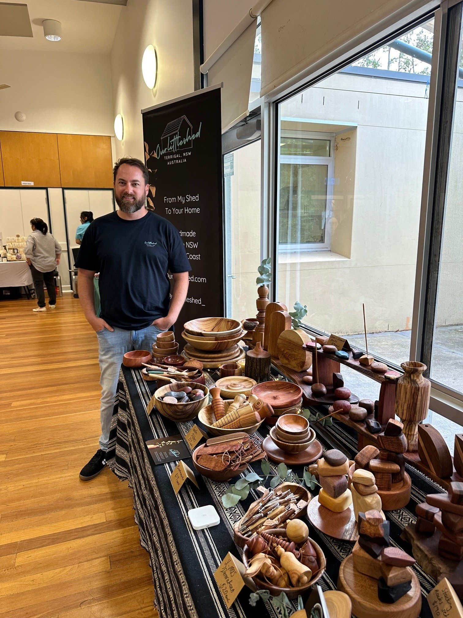 A man standing next to a display of handmade wooden crafts at an indoor market or event.