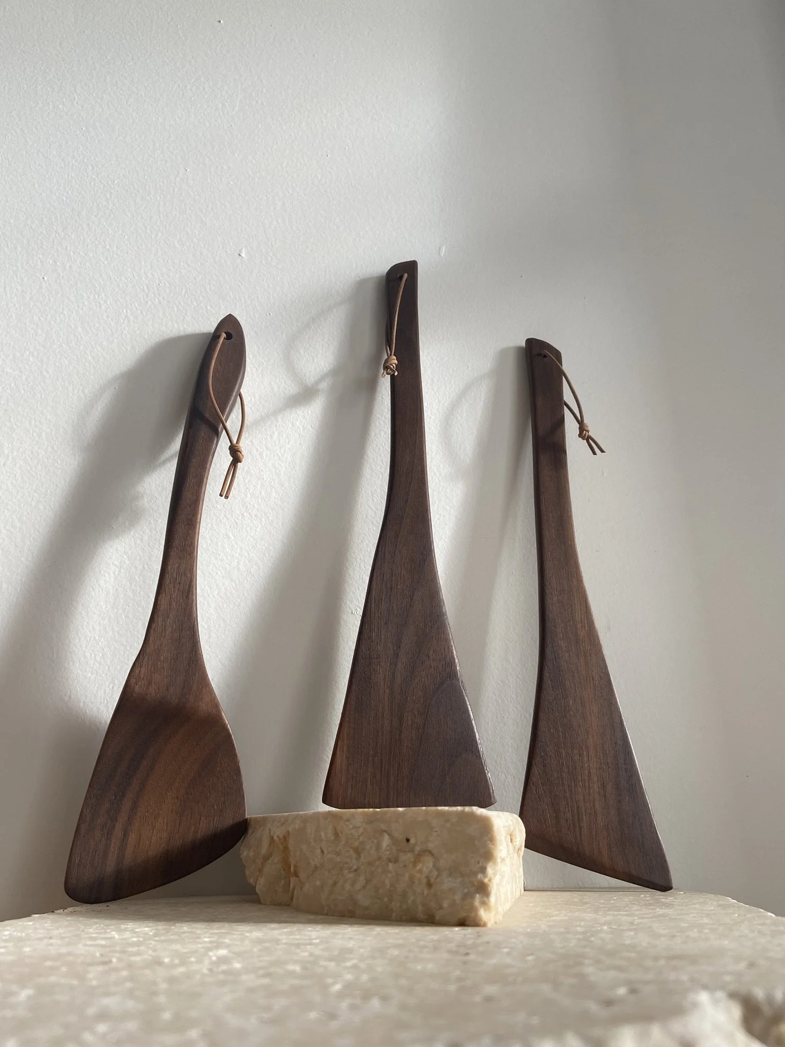 Three wooden decorative boats with string ties, placed on a stone against a plain white wall.