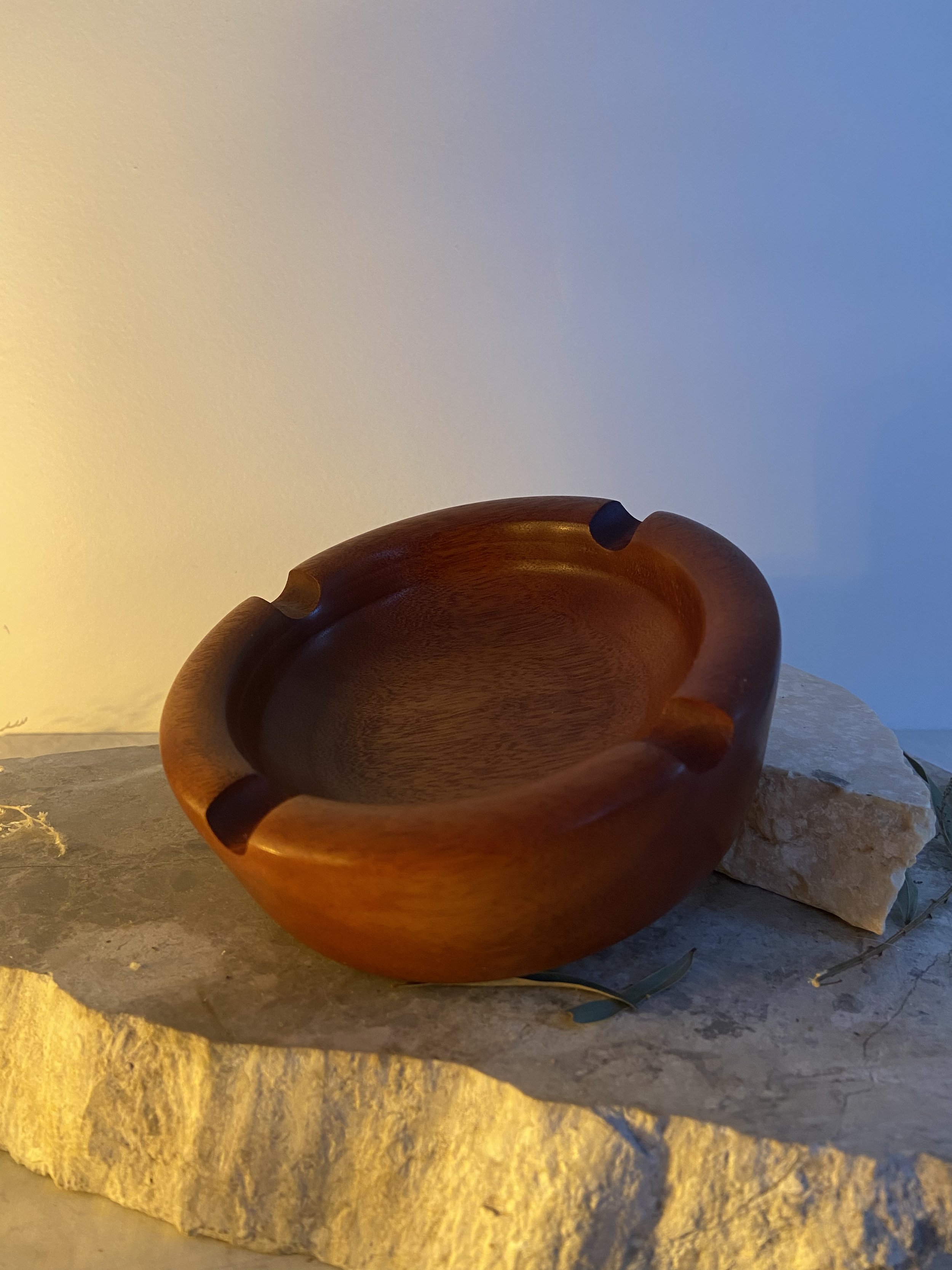 Wooden ashtray placed on a stone surface with a small green leaf nearby.