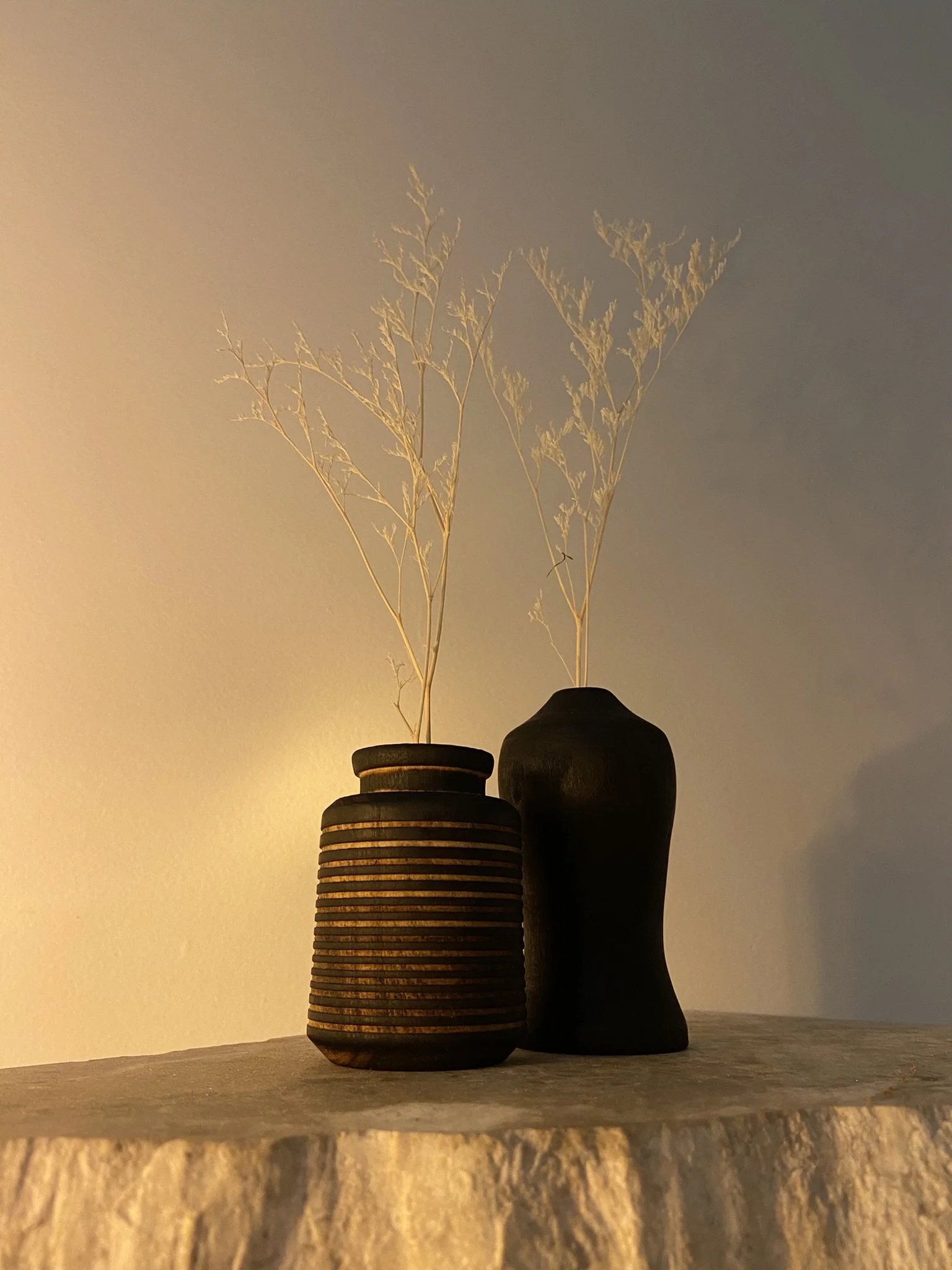Decorative black vases with dried white branches on a textured surface against a plain wall.