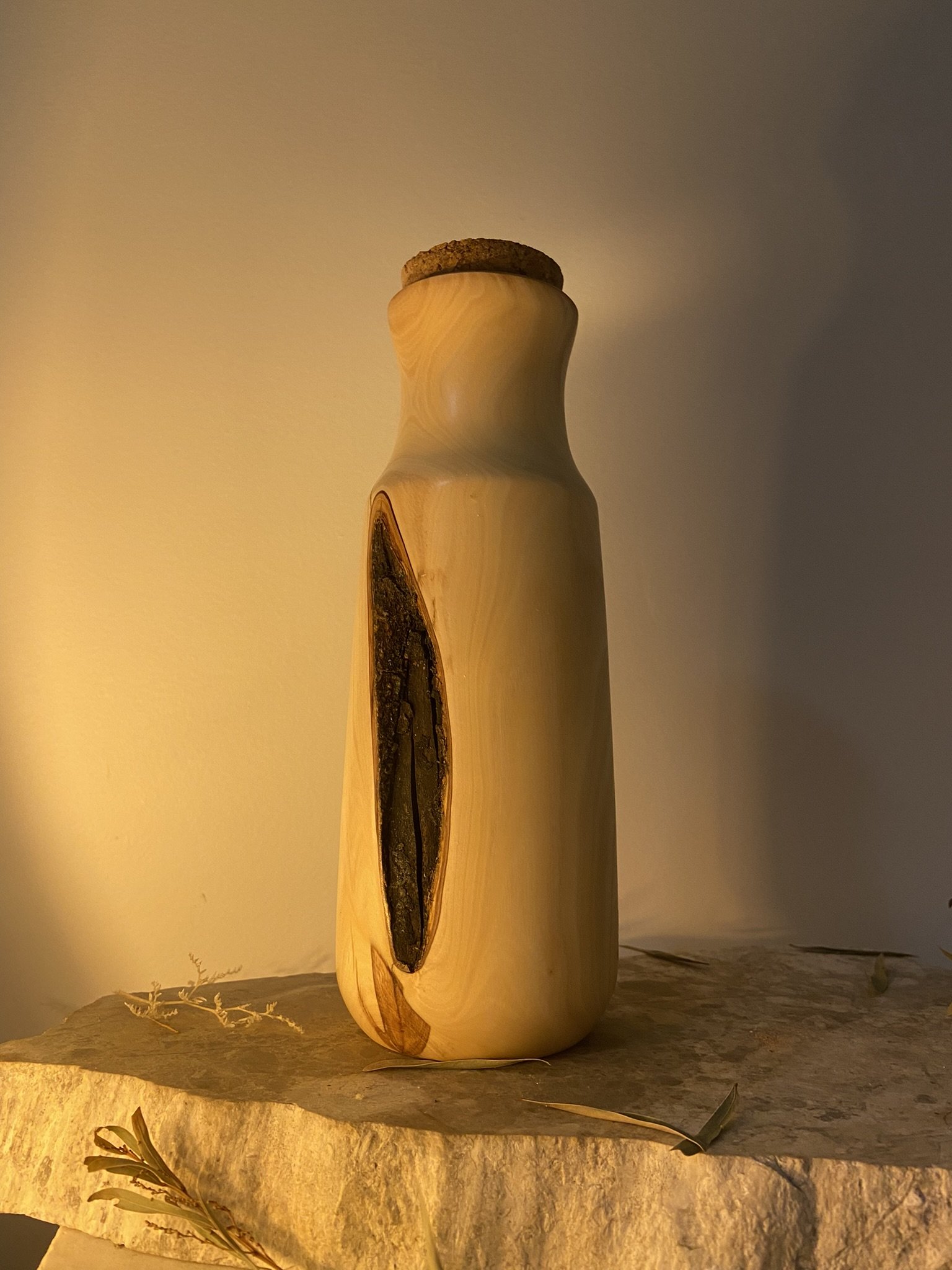 A wooden vase with a dark, elongated natural wood grain pattern, placed on a textured stone surface against a warm background.