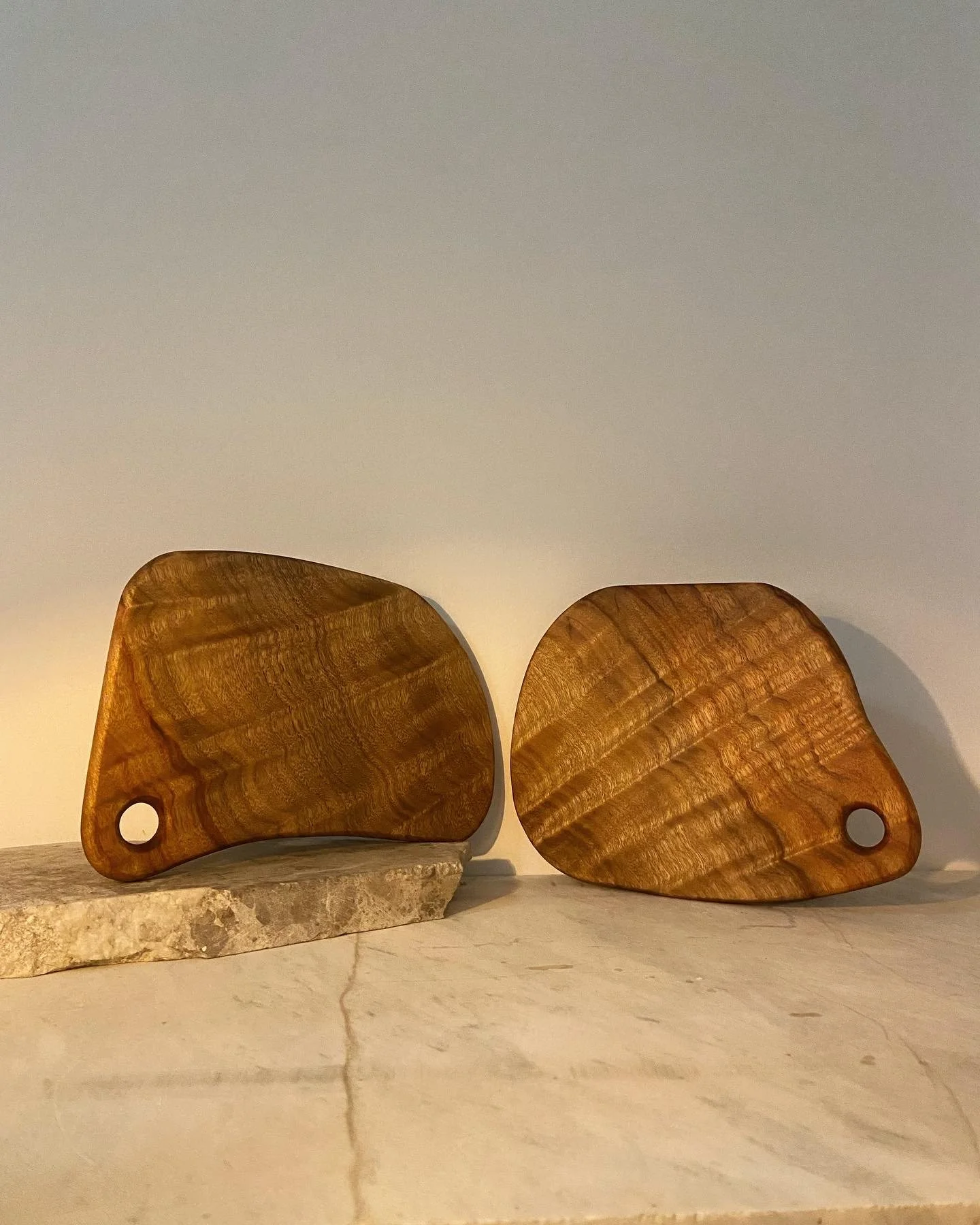 Two wooden cutting boards with a hole in one corner, placed on a stone and marble surface.