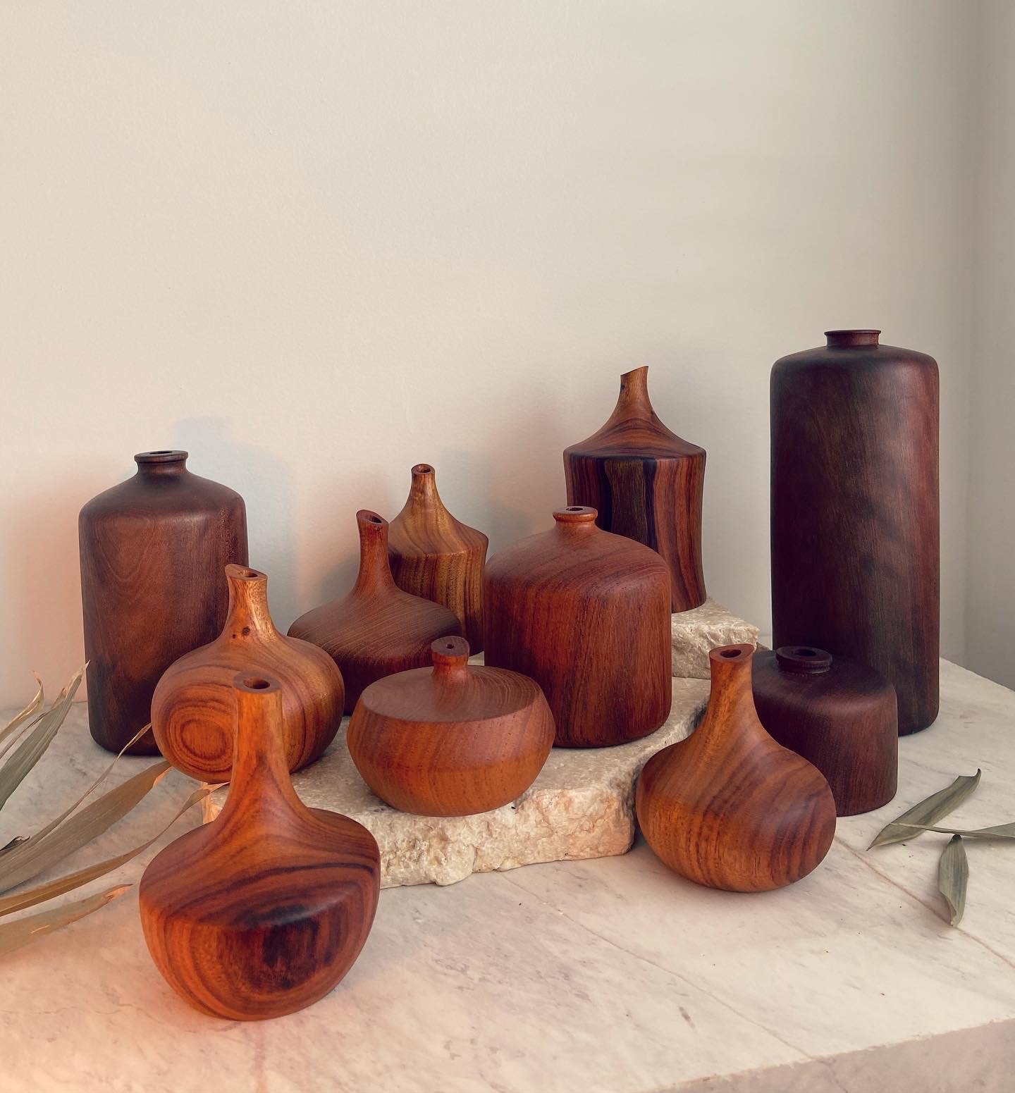 Collection of wooden vases of various shapes and sizes on a stone surface against a plain wall.