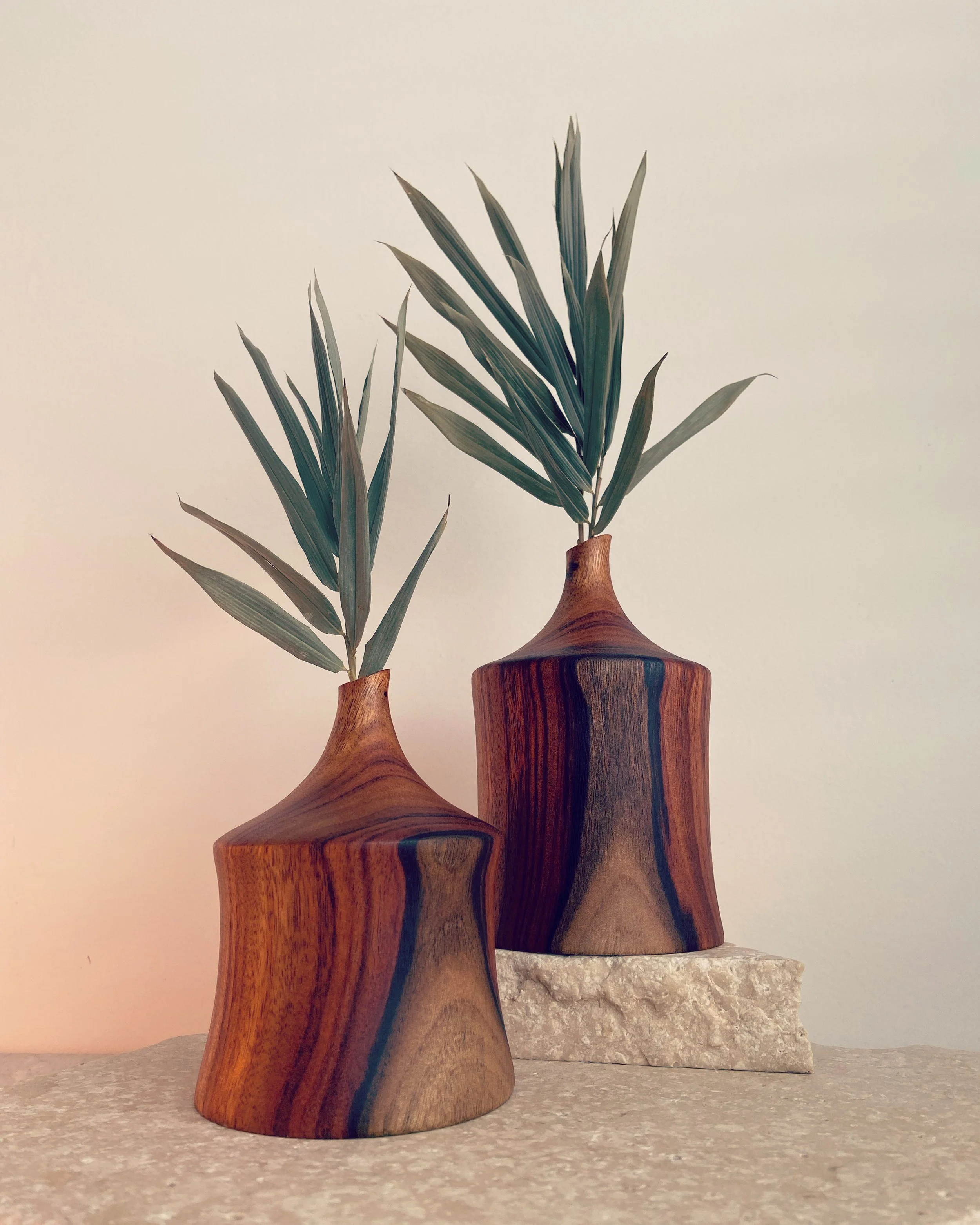 Two wooden vases with leaf arrangements on a textured surface, with a plain light background.