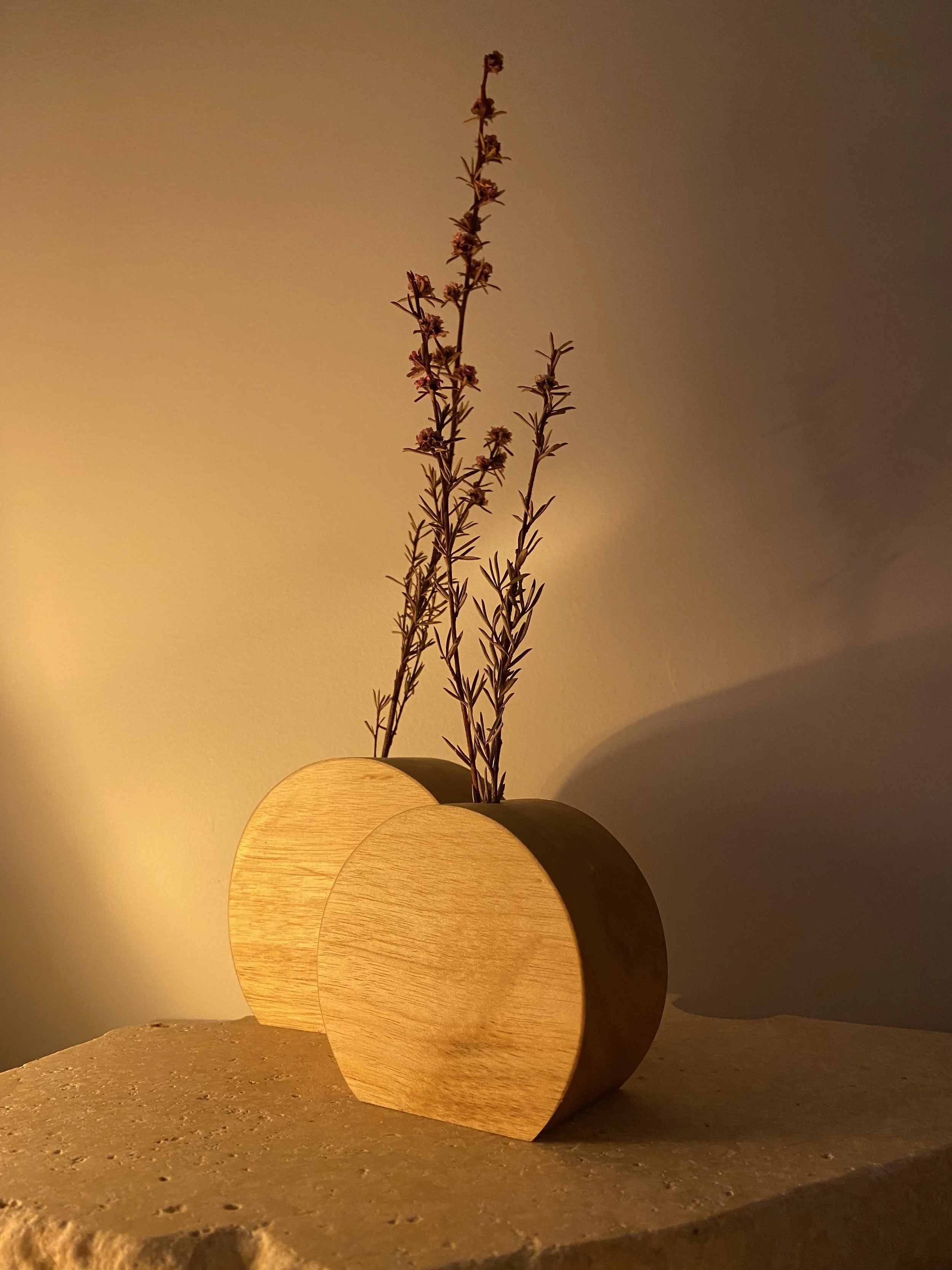 A wooden heart-shaped vase holding dried lavender stems on a textured surface against a warm-colored wall.