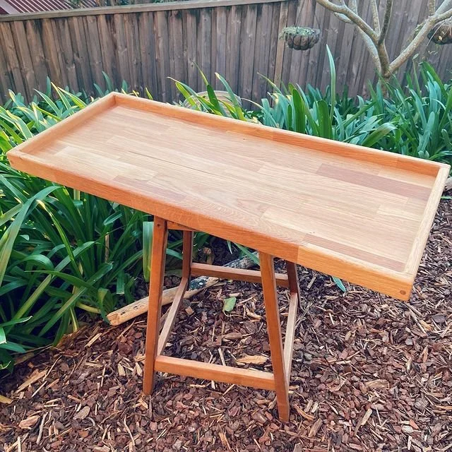 Wooden tabletop stand on a garden ground with green plants and a wooden fence in the background.