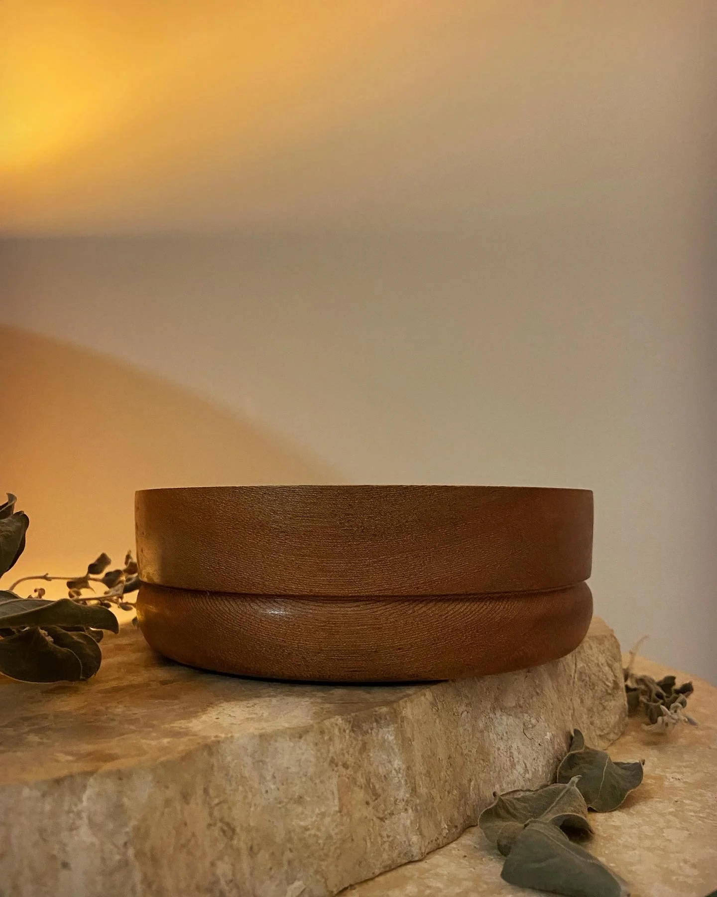 A round wooden bowl placed on a textured stone surface with dried leaves around it, soft warm lighting