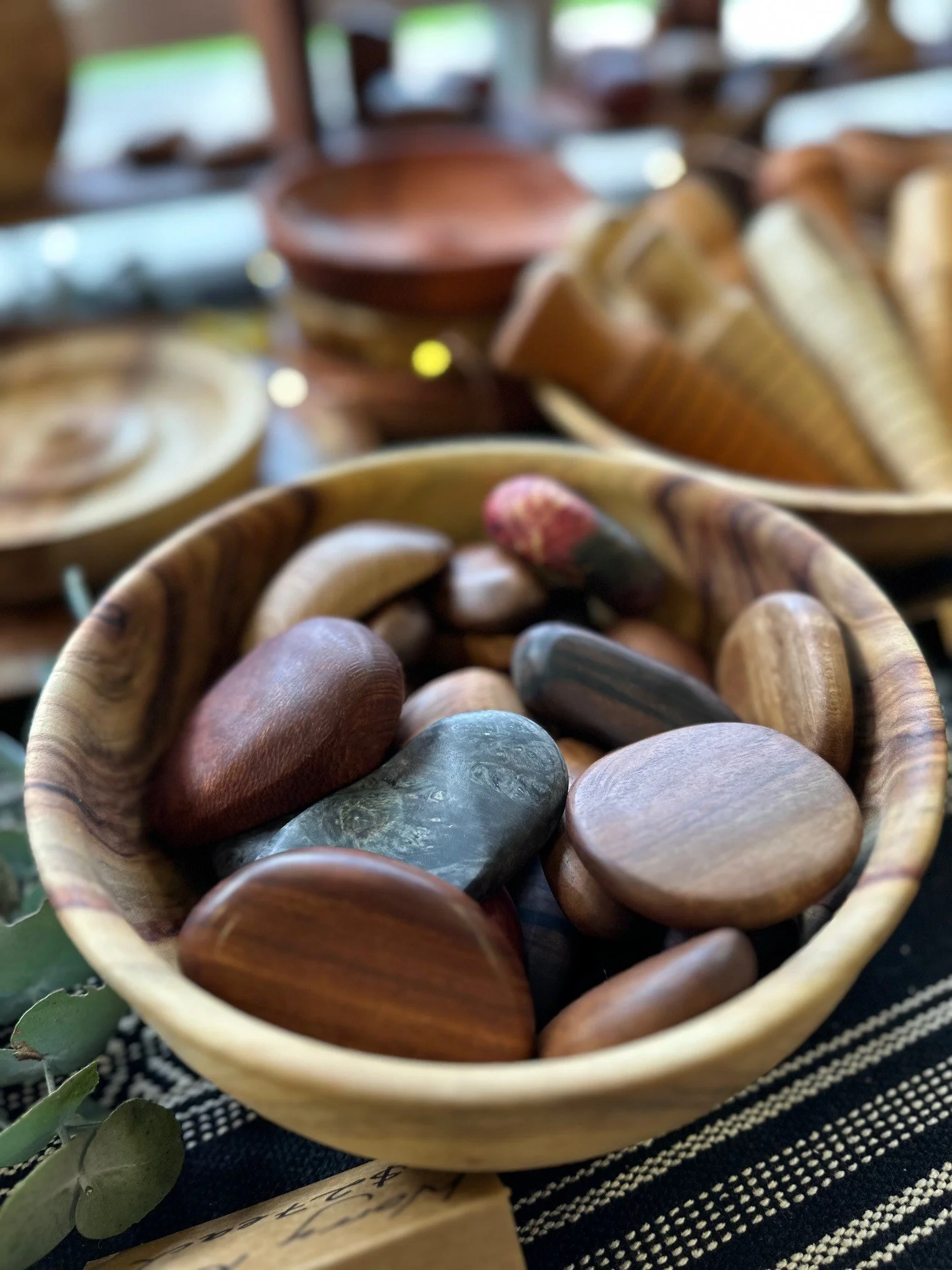 Various polished stones in a wooden bowl, with more bowls of stones and other items blurred in the background.