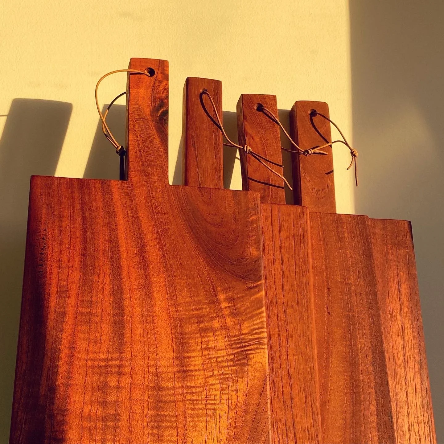 Wooden wall art piece with four vertical slats, each tied with a leather cord, mounted on a wall with sunlight casting shadows.