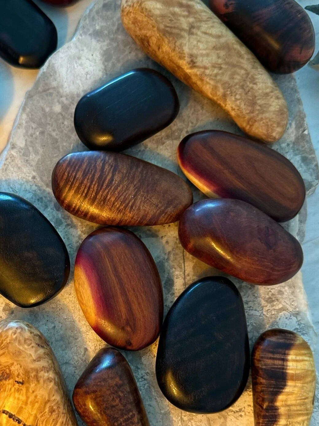 A collection of smooth, polished stones in black, brown, and reddish tones arranged on a stone surface.