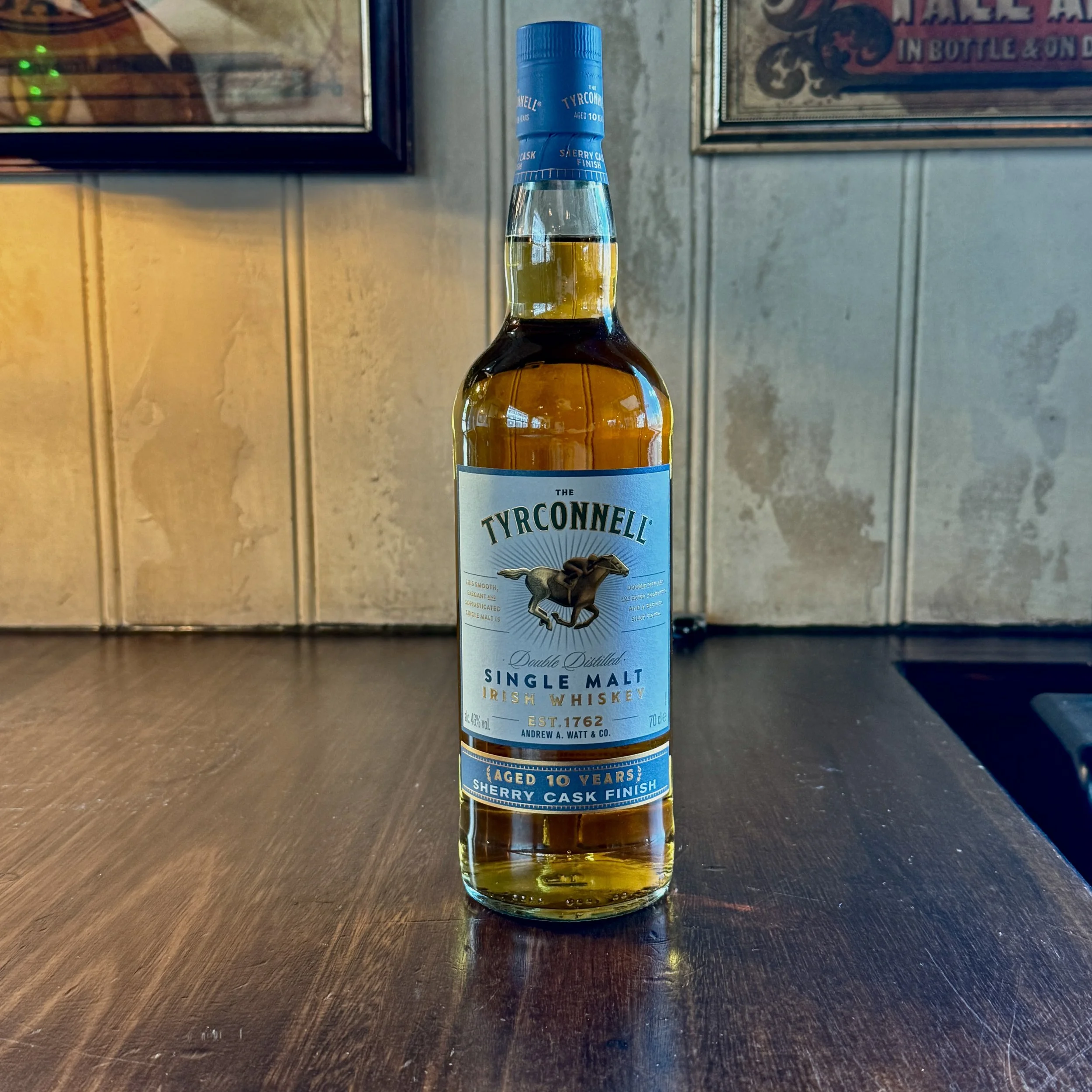 A bottle of TYRCONNELL Irish whiskey with a label indicating it is single malt, aged 10 years, with a Madeira cask finish, standing on a dark wooden surface.