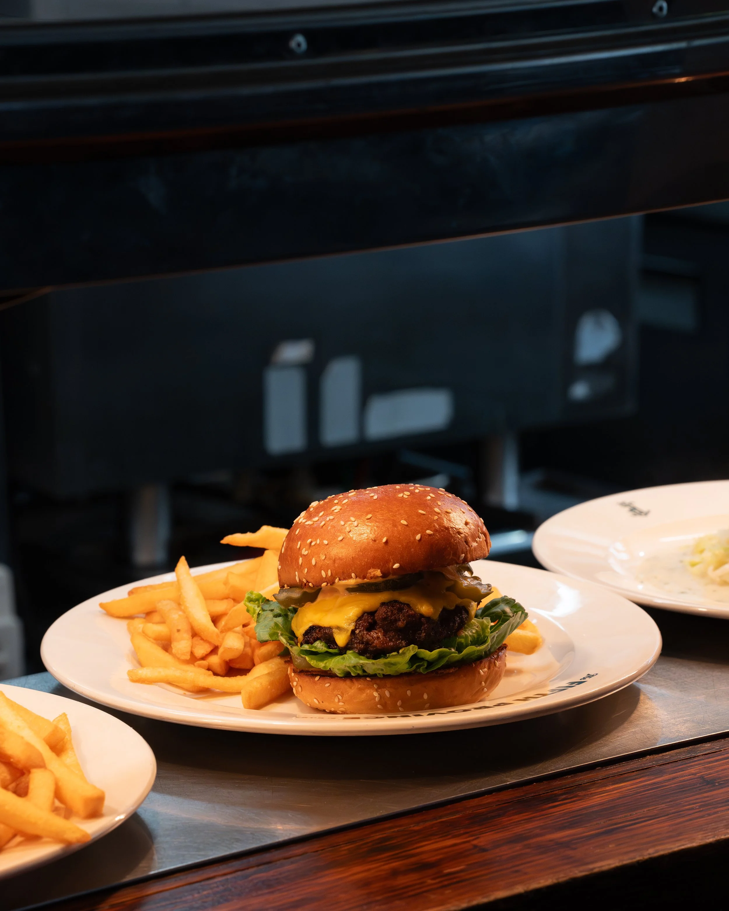 A cheeseburger with lettuce, pickles, cheddar cheese, and a sesame seed bun, served with French fries on a white plate.