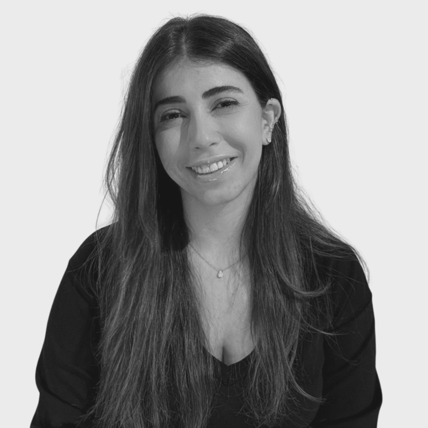 Black and white photo of a young woman with shoulder-length hair, wearing a black turtleneck sweater, smiling with one eye slightly closed against a plain light background.