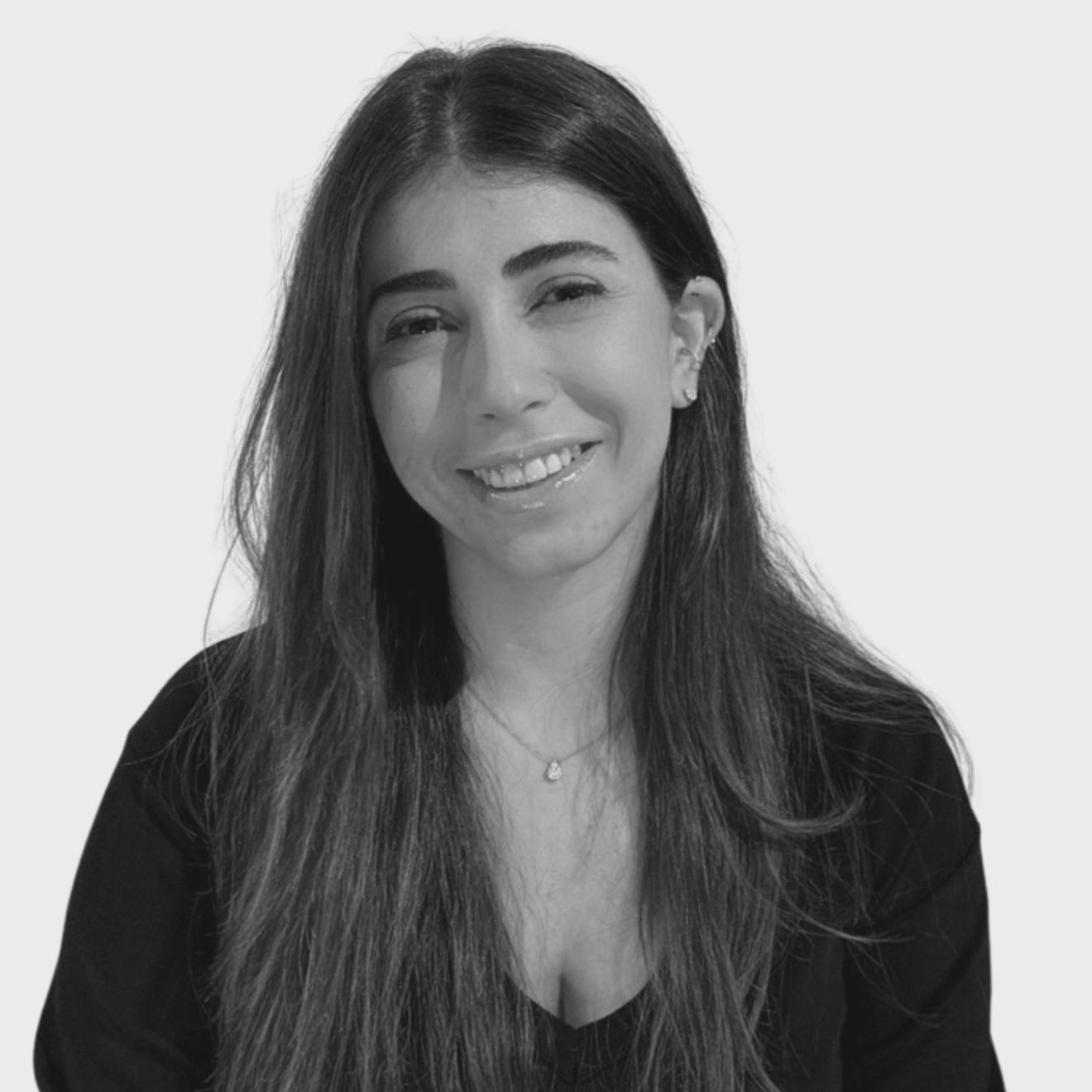 Black and white photo of a young woman with shoulder-length hair, wearing a black turtleneck sweater, smiling with one eye slightly closed against a plain light background.